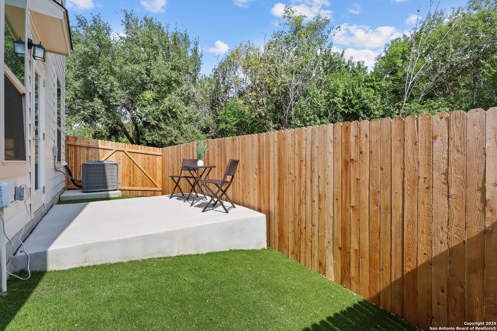 Private backyard with wooden privacy fence, artificial turf grass, and concrete patio bistro set in Cedar Heights, San Antonio, Texas