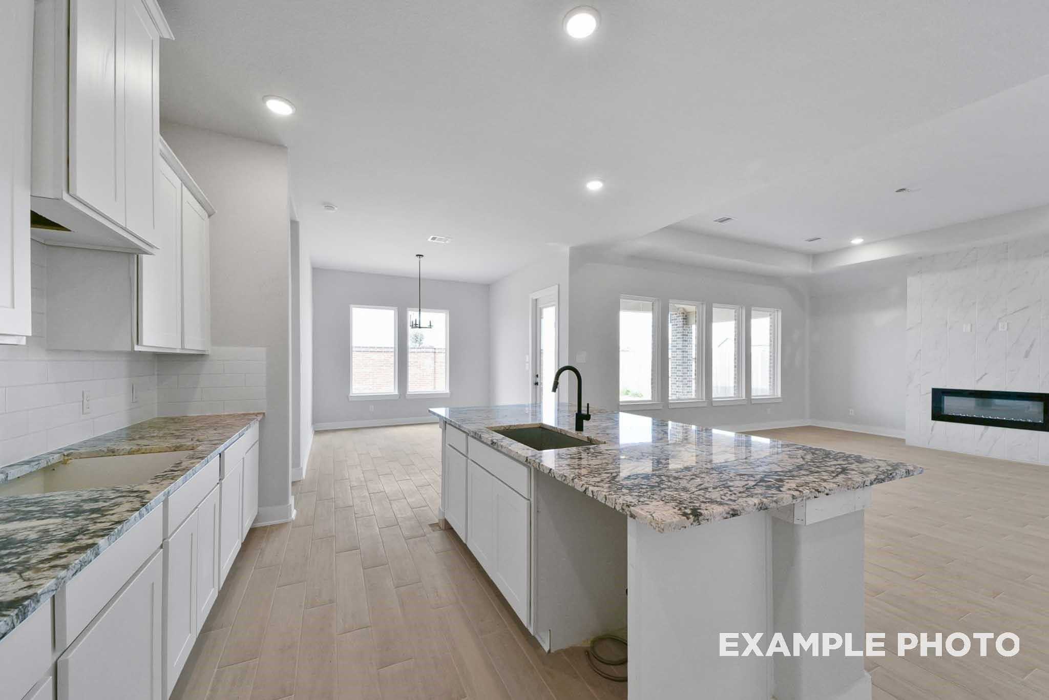 Modern open-concept kitchen with white shaker cabinets, speckled granite island sink, and gas fireplace living area in Davidson Homes The George A, Texas City