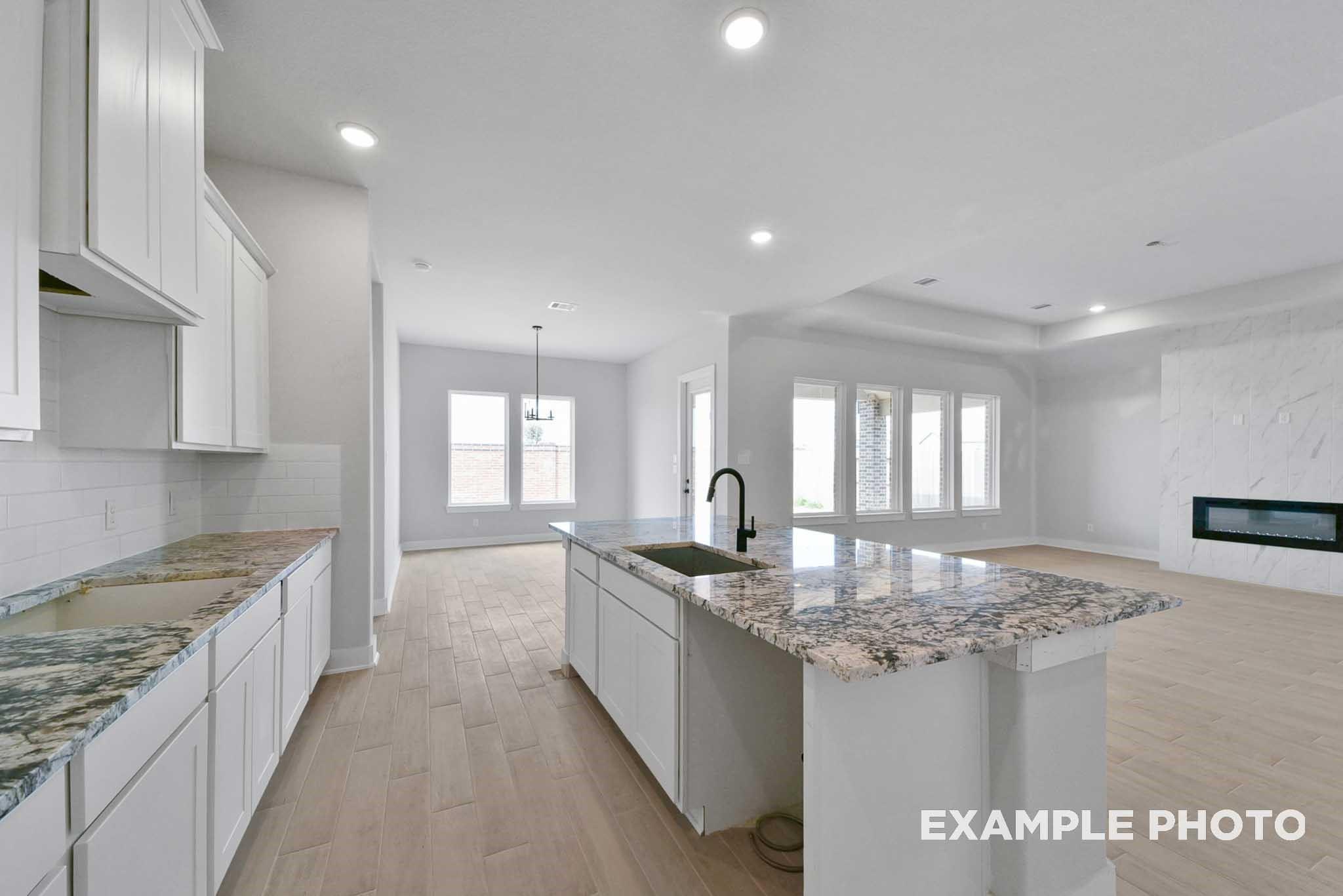 Modern open-concept kitchen with white shaker cabinets, speckled granite island sink, and gas fireplace living area in Davidson Homes The George A, Texas City
