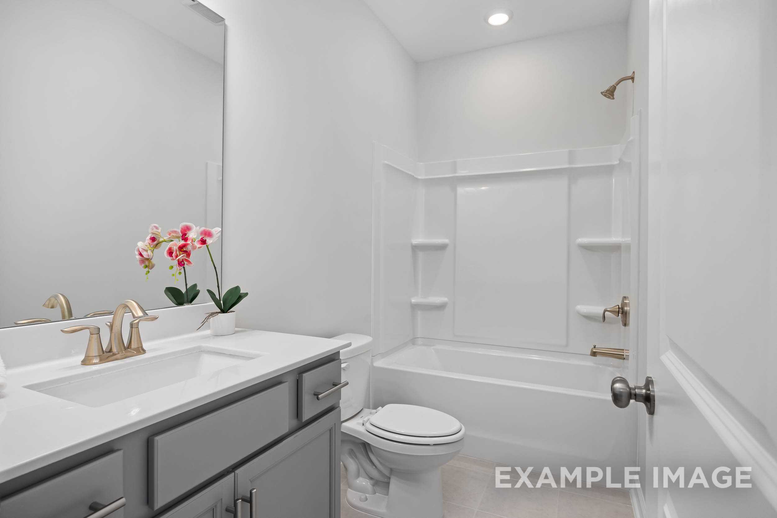 Spacious secondary bathroom in The Daphne C with white subway tile tub-shower, gold fixtures, gray vanity, and pink orchids