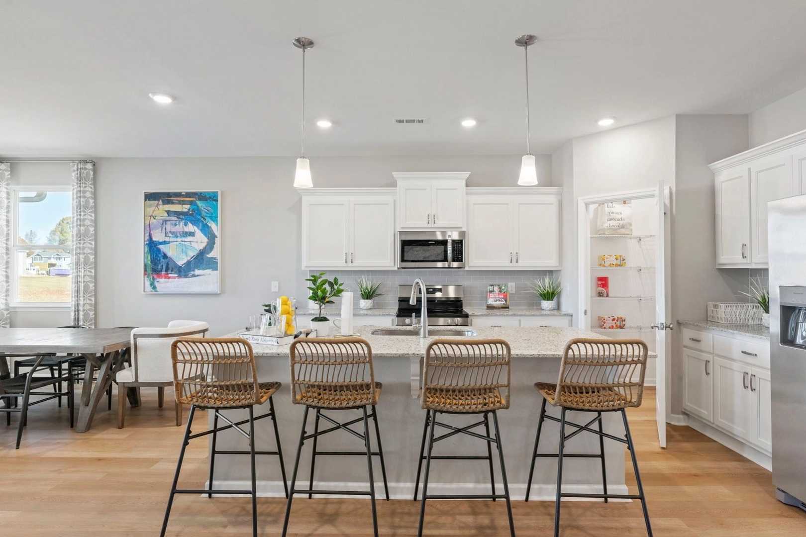 Spacious open-concept kitchen in Bailey Park home featuring white cabinets, large island with rattan stools, stainless appliances, and hardwood floors in Fayetteville, TN