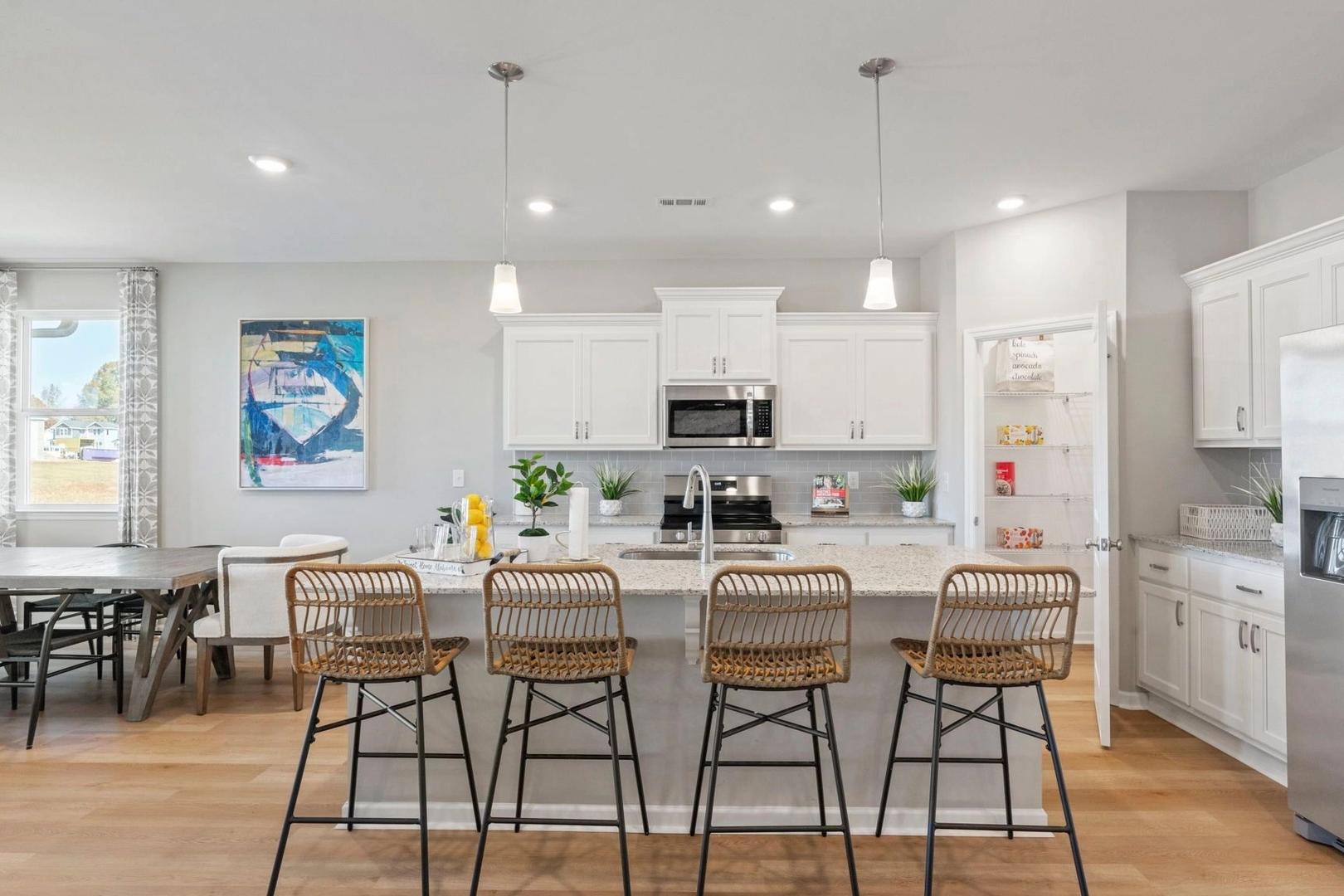 Spacious open-concept kitchen in Bailey Park home featuring white cabinets, large island with rattan stools, stainless appliances, and hardwood floors in Fayetteville, TN