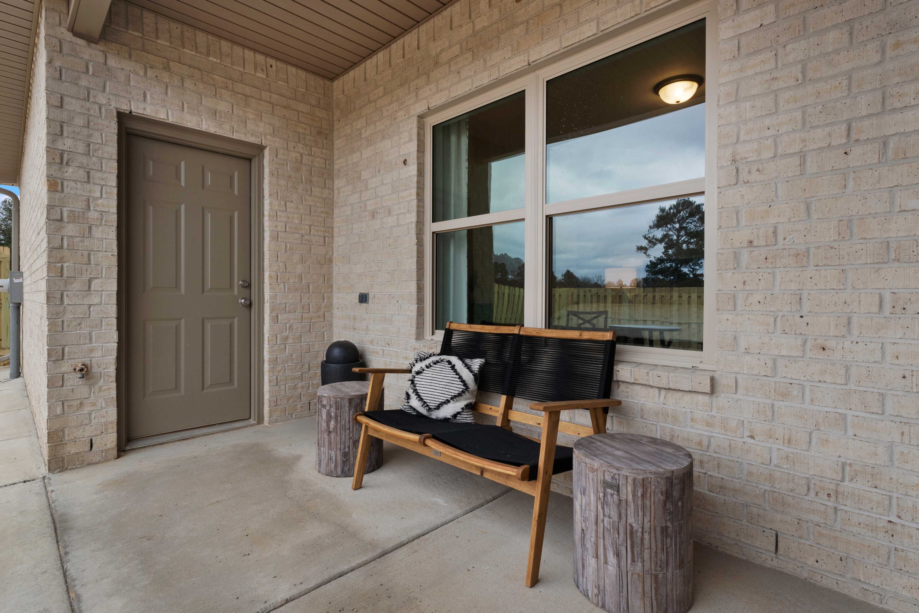 Covered front porch with wooden bench, stump tables, beige brick exterior and large windows at The Retreat at Cain Park in Hartselle, Alabama