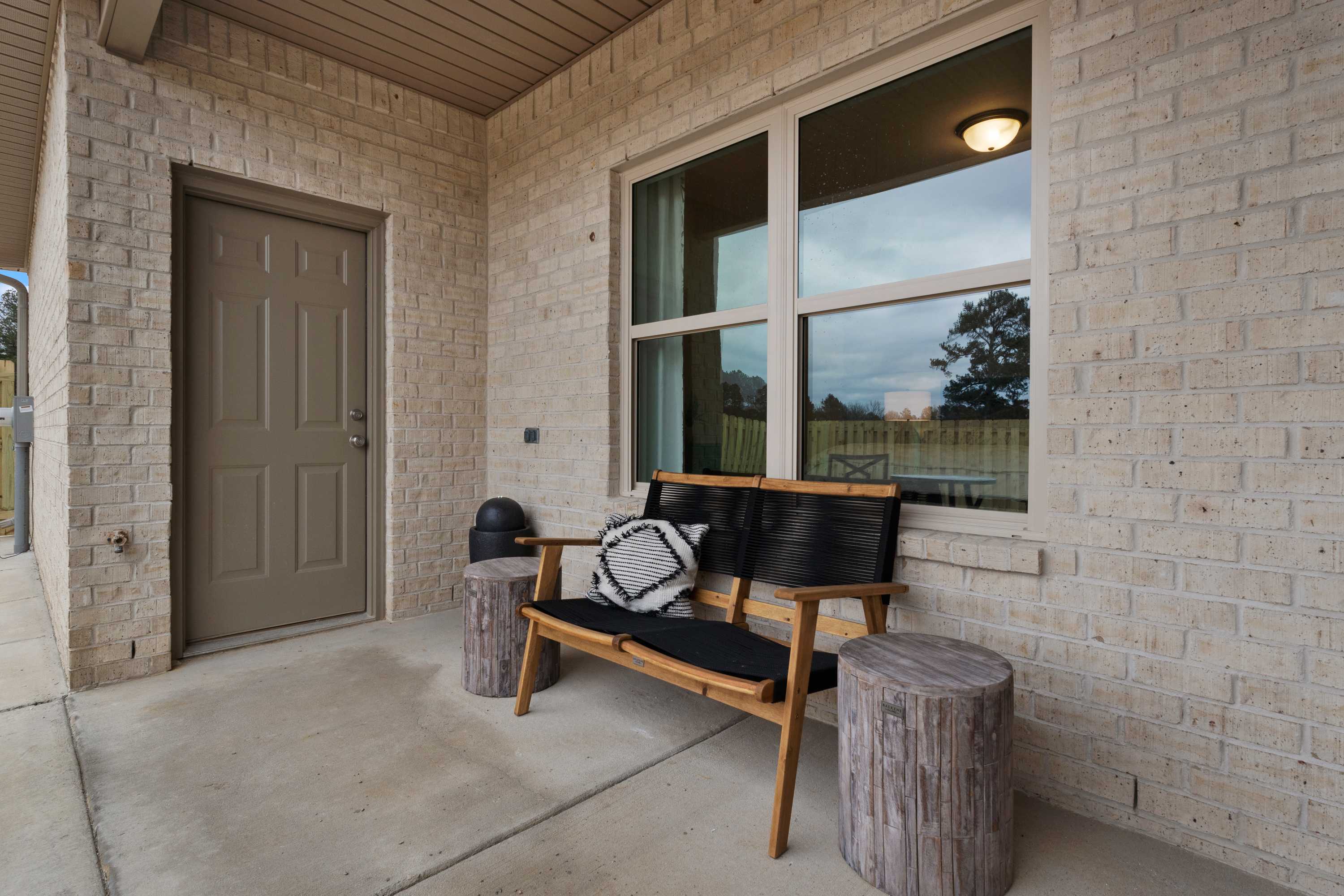 Covered front porch with wooden bench, stump tables, beige brick exterior and large windows at The Retreat at Cain Park in Hartselle, Alabama