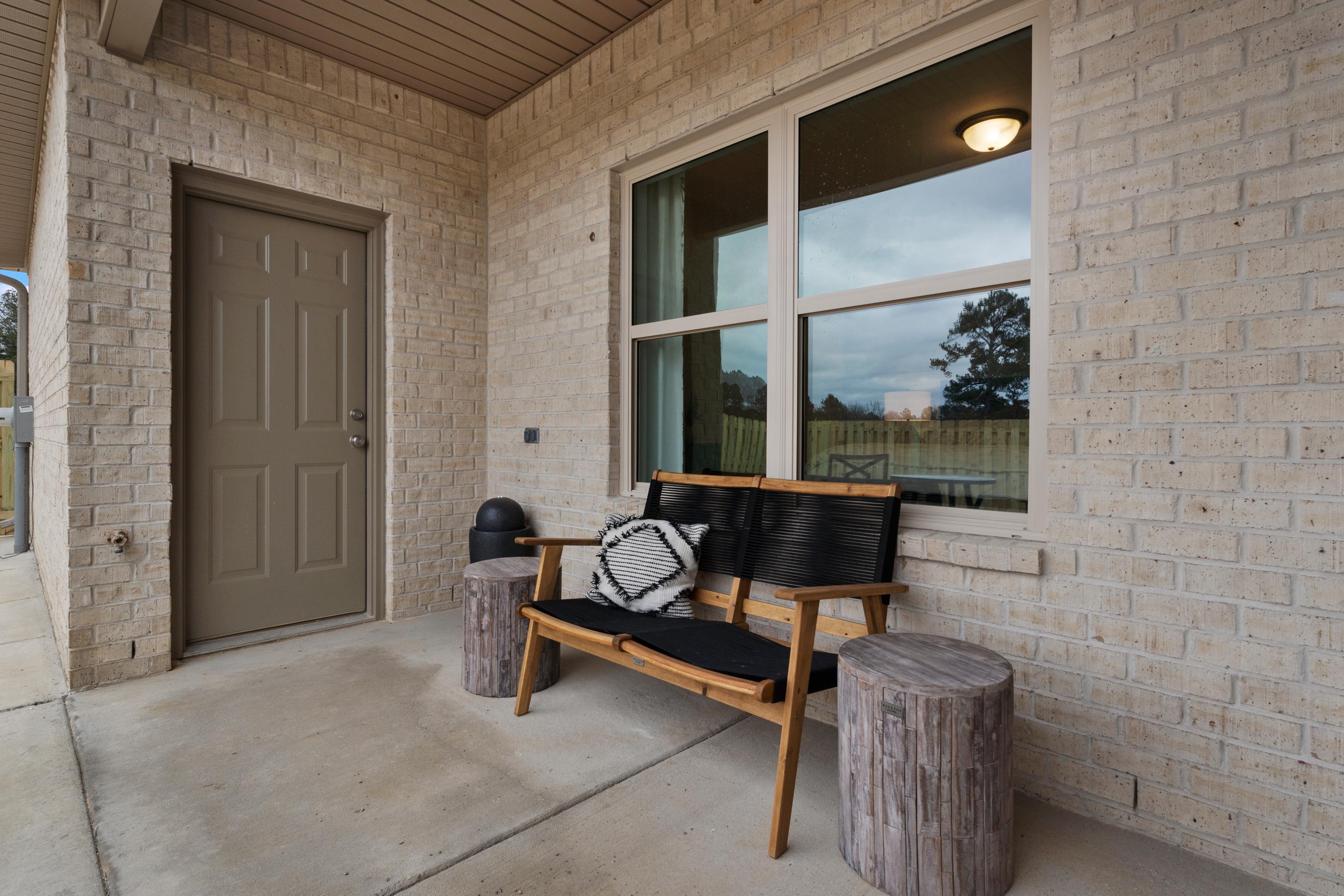 Covered front porch with wooden bench, stump tables, beige brick exterior and large windows at The Retreat at Cain Park in Hartselle, Alabama