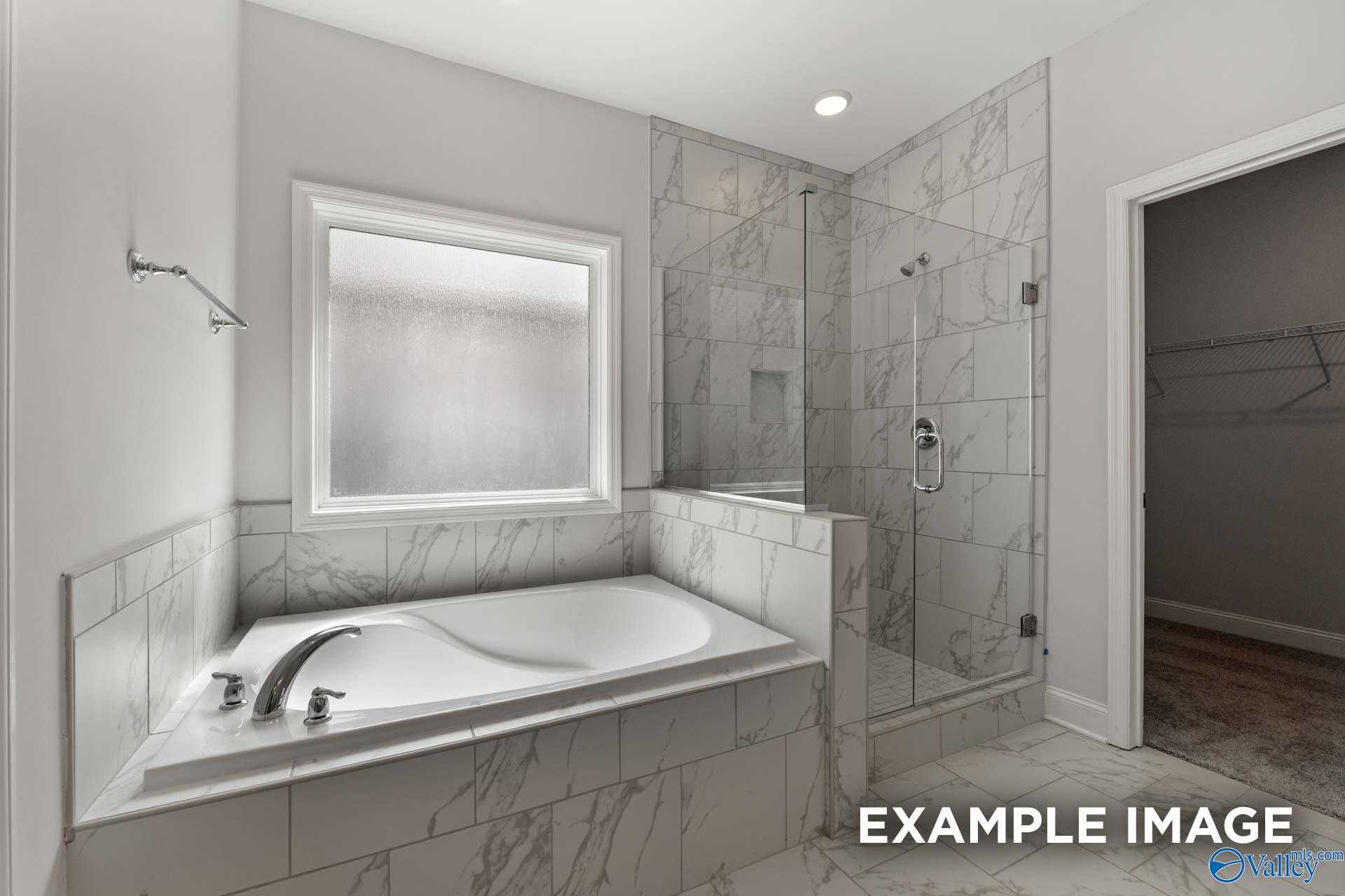 Elegant master bath with freestanding soaking tub, marble tiles, glass shower enclosure, frosted window in Davidson Homes Harrison B, Decatur AL
