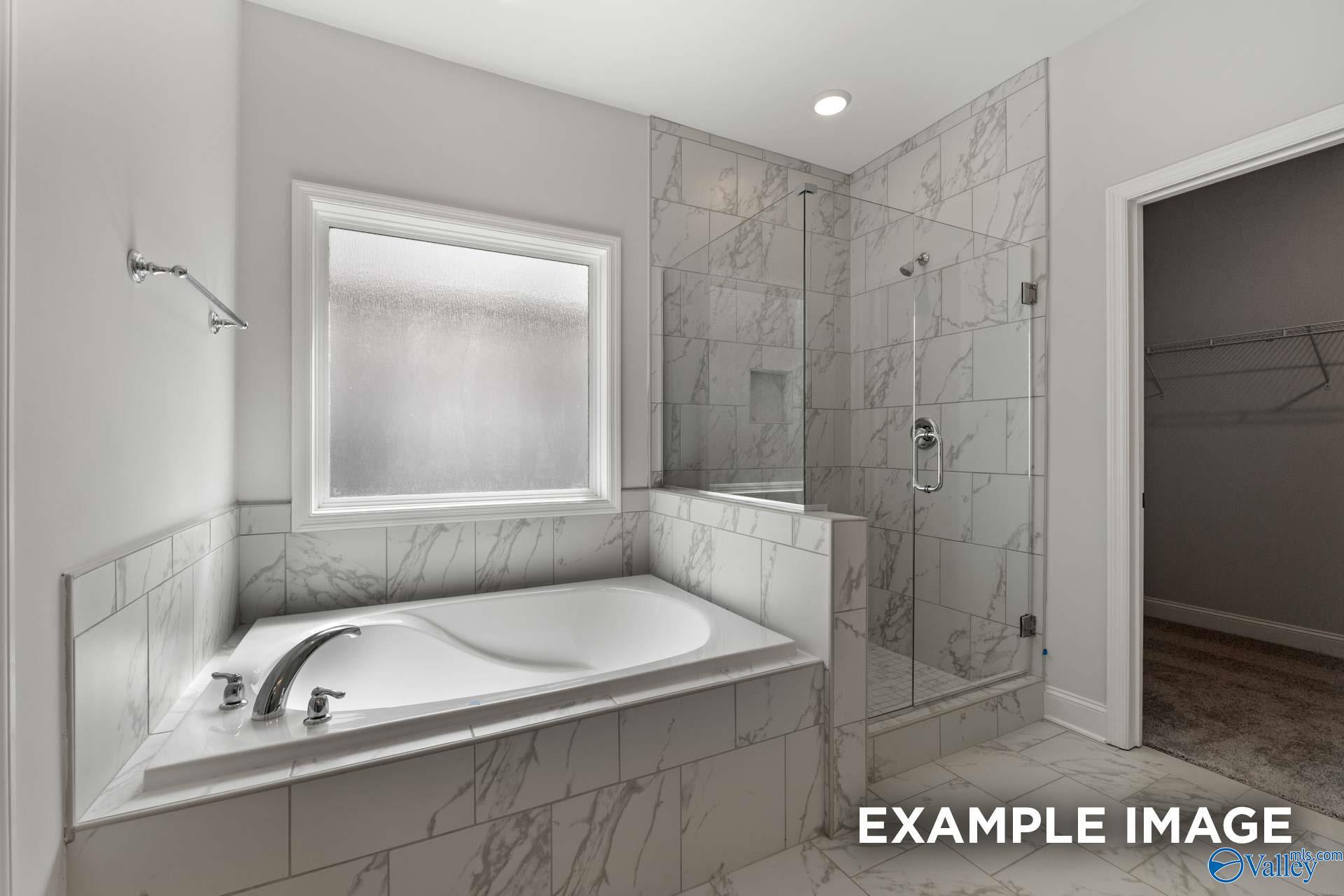 Elegant master bath with freestanding soaking tub, marble tiles, glass shower enclosure, frosted window in Davidson Homes Harrison B, Decatur AL