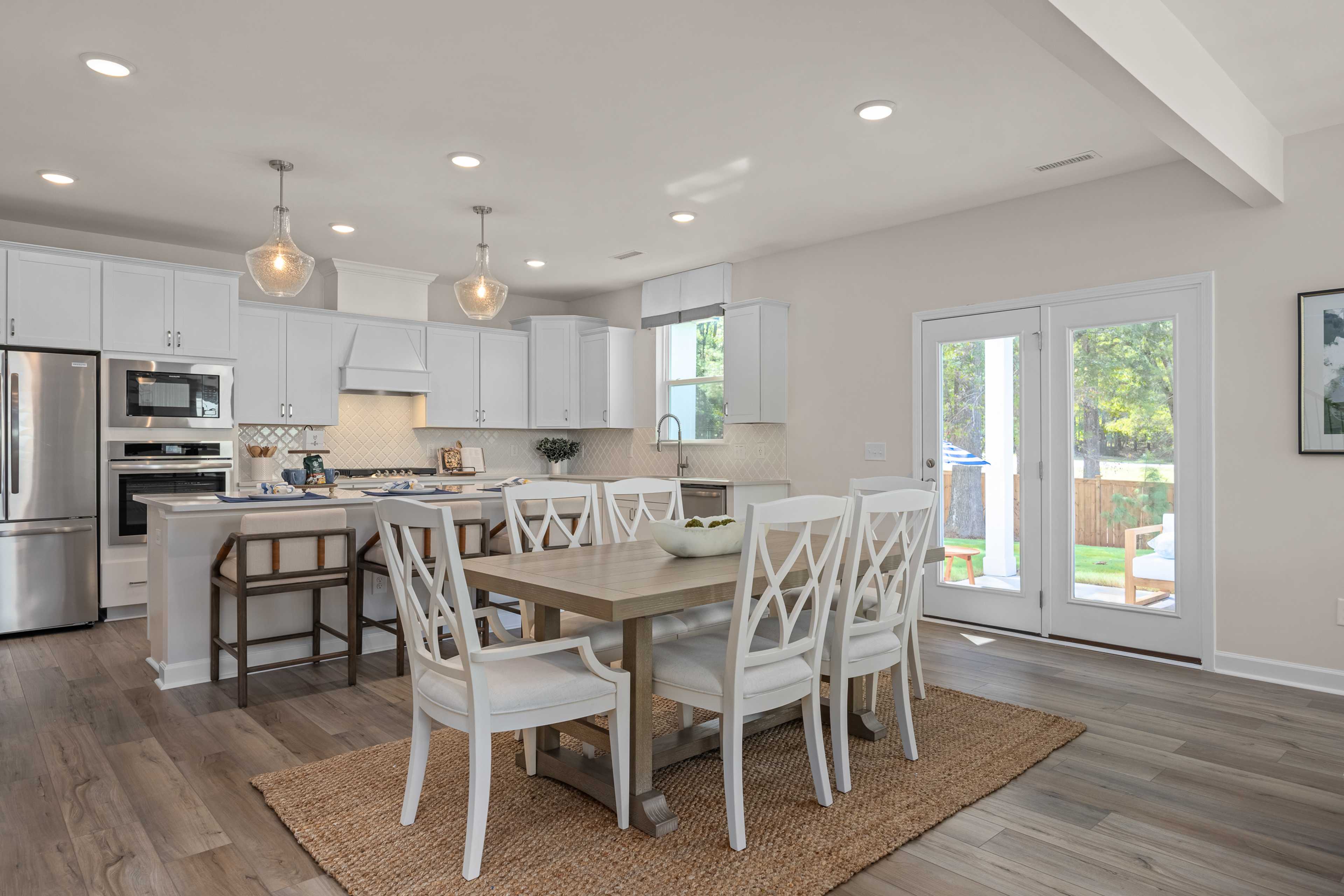 Open-concept kitchen and dining at Sage on North Main in Wake Forest NC with white cabinets, island bar, hardwood floors, and French doors