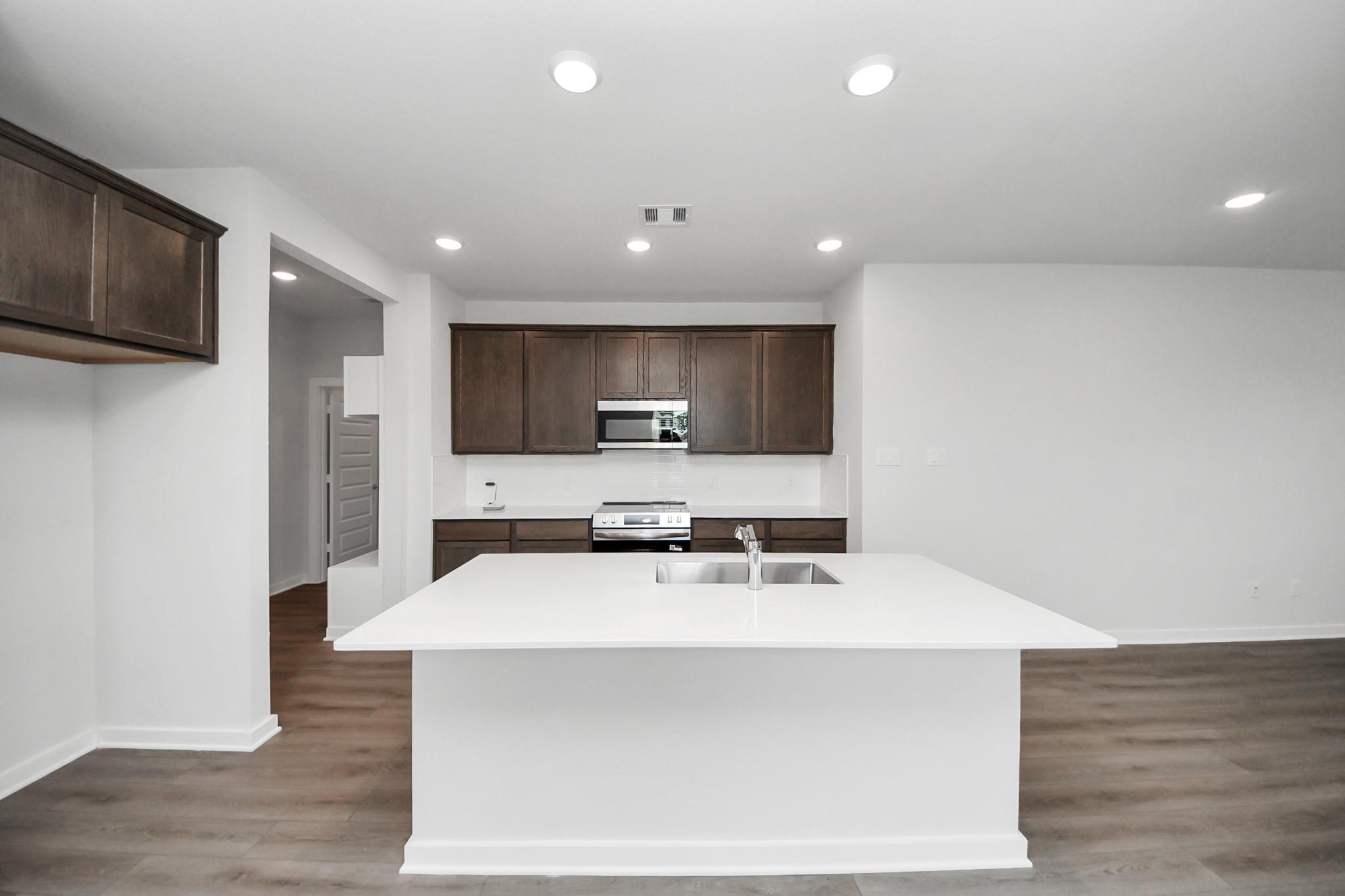 Modern kitchen with white island, dark wood cabinets, and stainless appliances in Brazos F plan at Liberty Estates, TX.