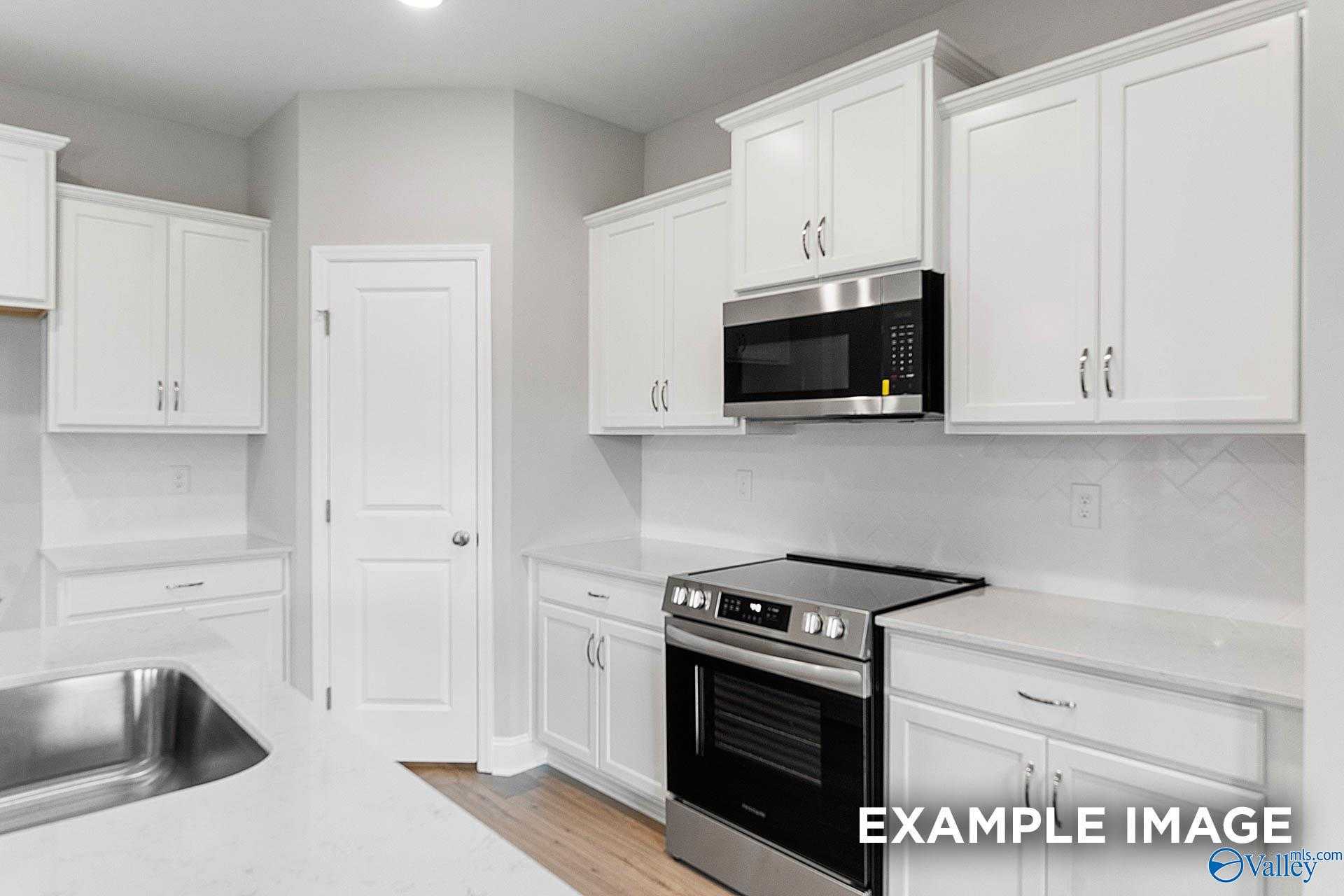 Modern white kitchen with stainless steel oven, microwave, and farmhouse sink in Davidson Homes The Franklin E, Hazel Green, AL