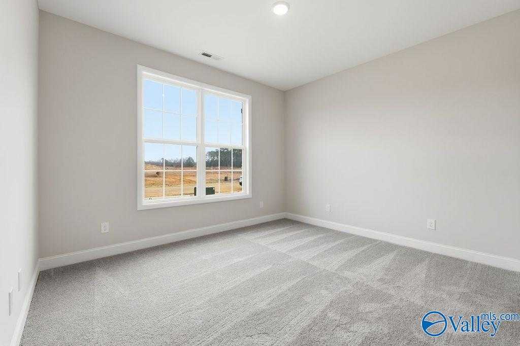 Bright empty bedroom with large window overlooking rural fields, neutral gray walls, and plush carpet in Davidson Homes The Rockford B, Hartselle, Alabama