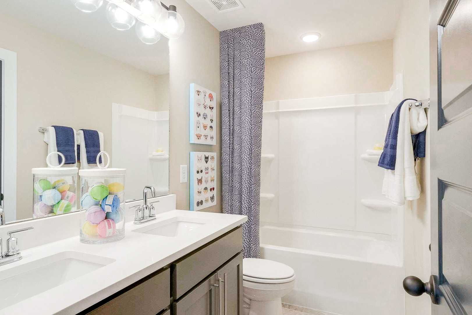 Bright family bathroom at The Meadows in Smyrna TN by Davidson Homes with double vanity, colorful jars, bathtub, and blue accents