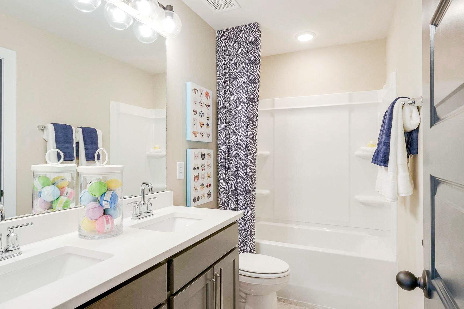 Bright family bathroom at The Meadows in Smyrna TN by Davidson Homes with double vanity, colorful jars, bathtub, and blue accents