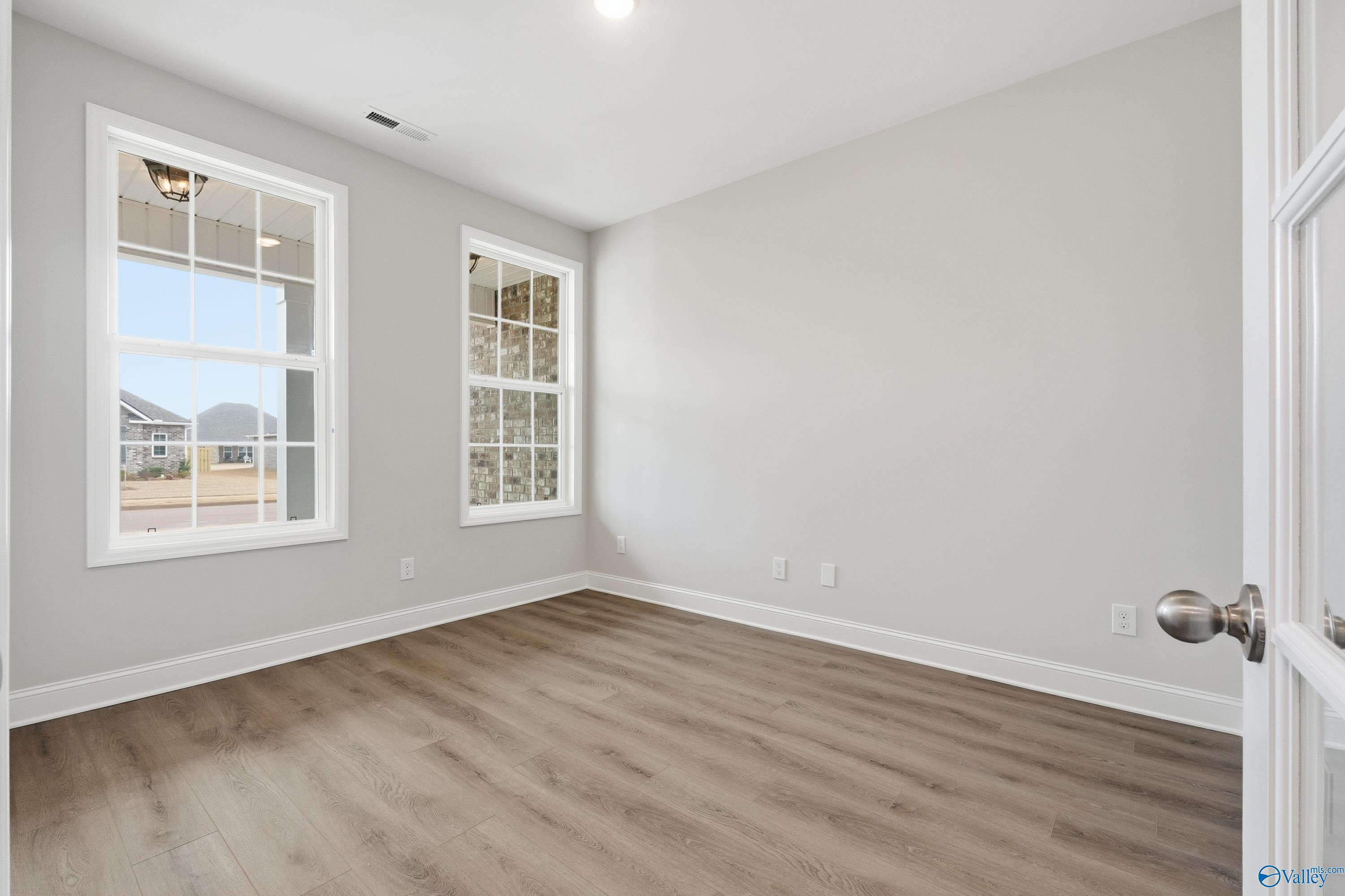 Bright bedroom with large windows overlooking neighborhood, hardwood floors, and neutral walls in Davidson Homes The Rockford, Meridianville