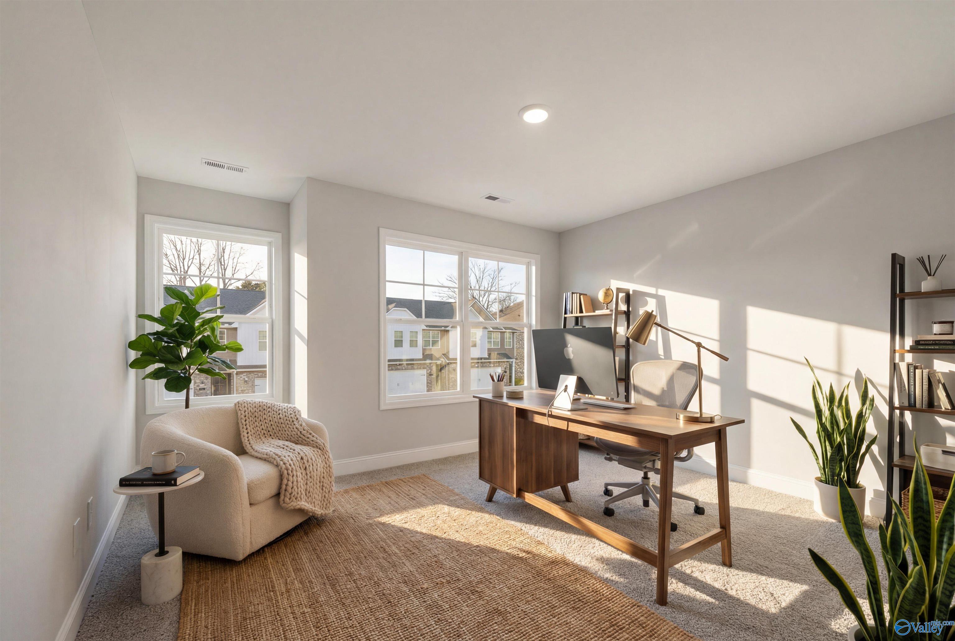 Cozy home office with wooden desk, ergonomic chair, bookshelves, armchair, plants, and natural light in Davidson Homes The Camden, Huntsville, Alabama