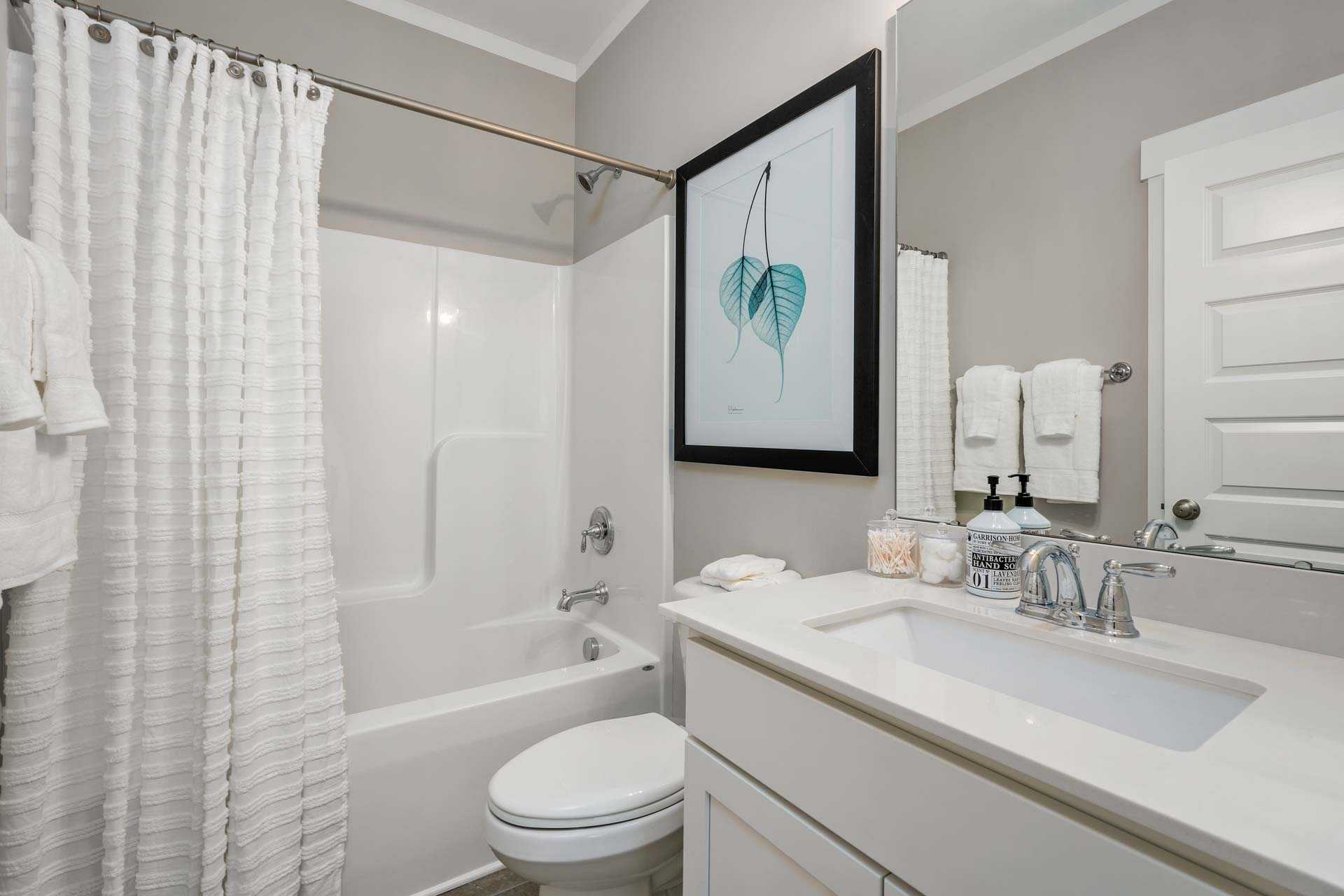 Spacious bathroom in Kendall Downs Toney Alabama with white tub shower combo vanity and leaf wall art
