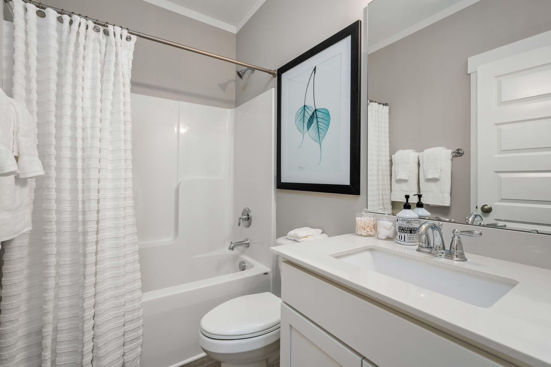 Spacious bathroom in Kendall Downs Toney Alabama with white tub shower combo vanity and leaf wall art