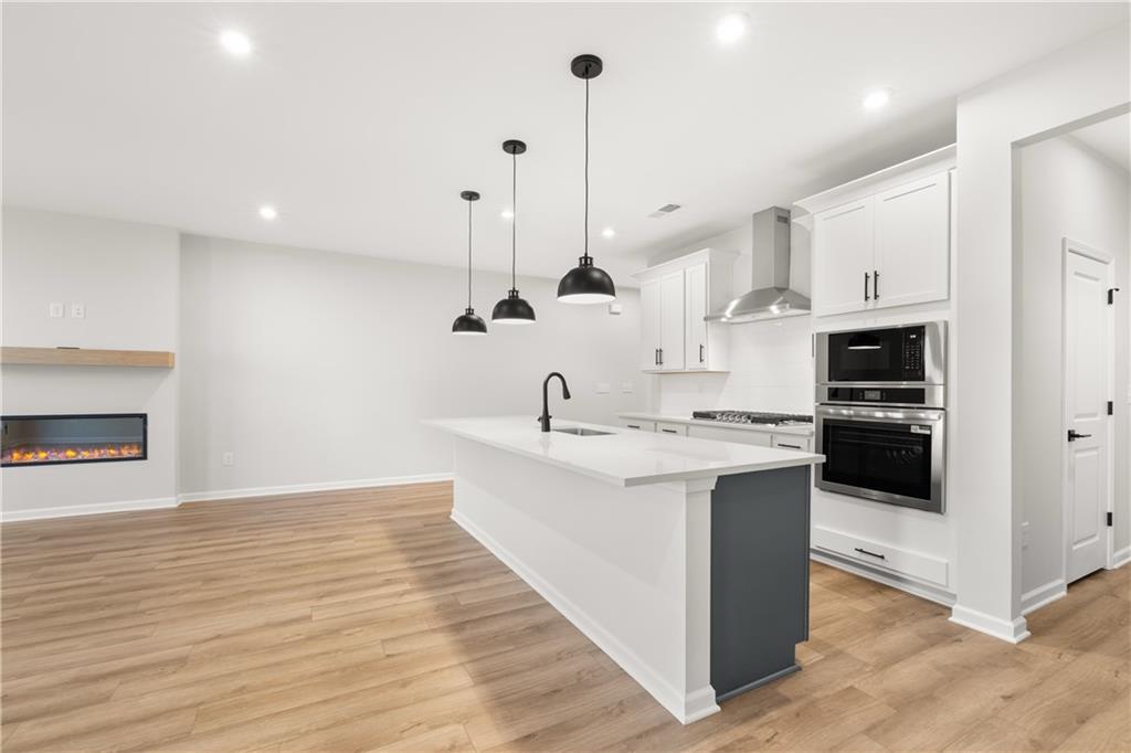 Modern open kitchen with white quartz island, stainless appliances, pendant lights, and linear gas fireplace in Davidson Homes The Cary A, Winder, Georgia