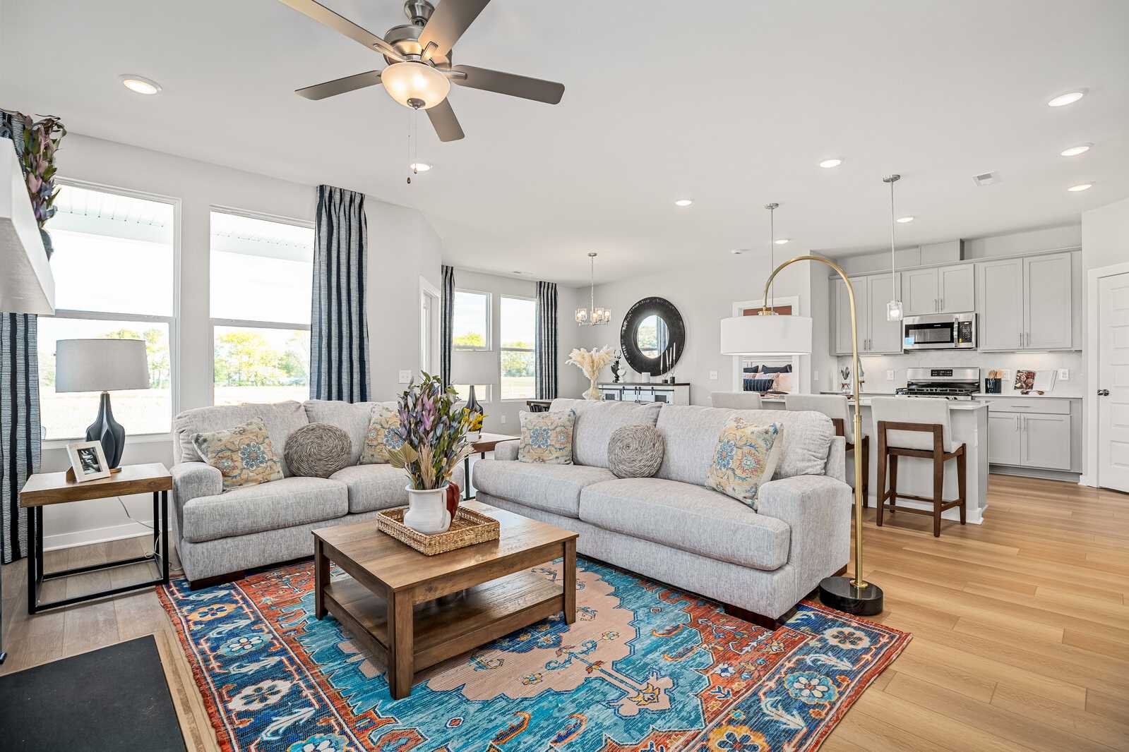 Open-concept living room and kitchen in Sage Farms, White House TN with gray sofas, hardwood floors, ceiling fan, and pendant lights