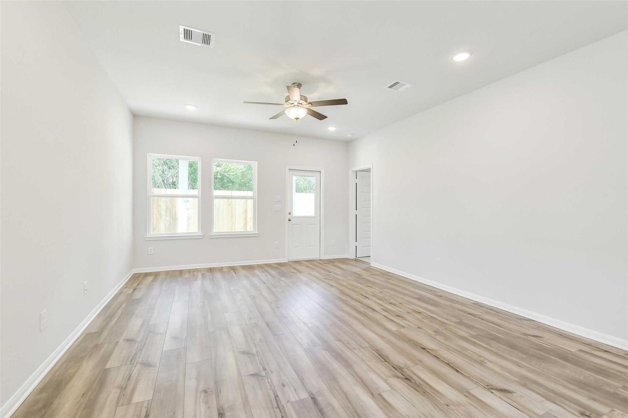 Spacious living room with light hardwood floors, ceiling fan, large windows, and back door in Davidson Homes Sabine E, Conroe, Texas
