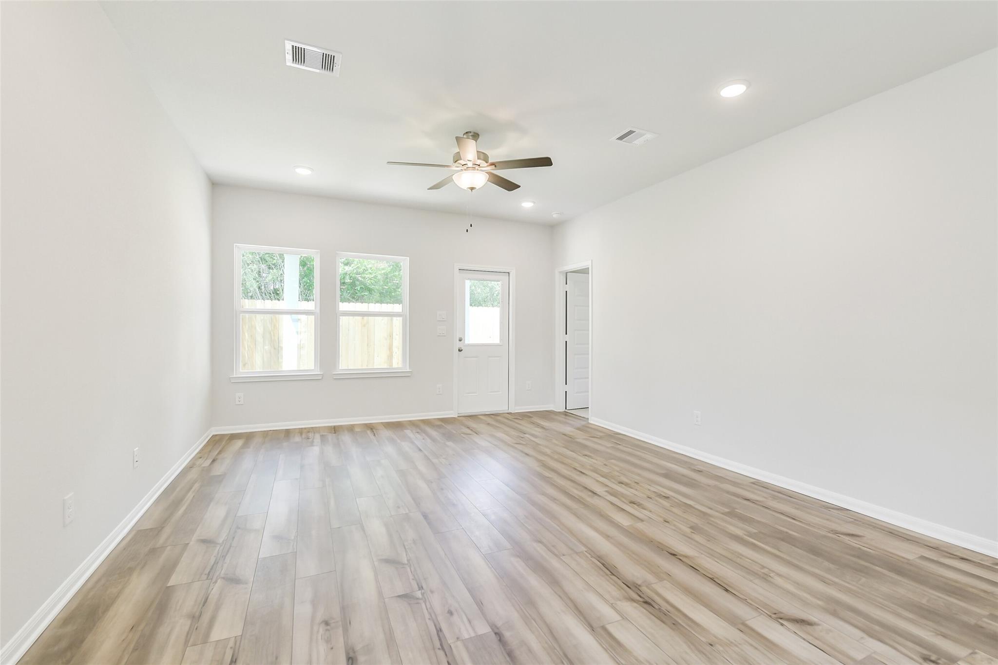 Spacious living room with light hardwood floors, ceiling fan, large windows, and back door in Davidson Homes Sabine E, Conroe, Texas