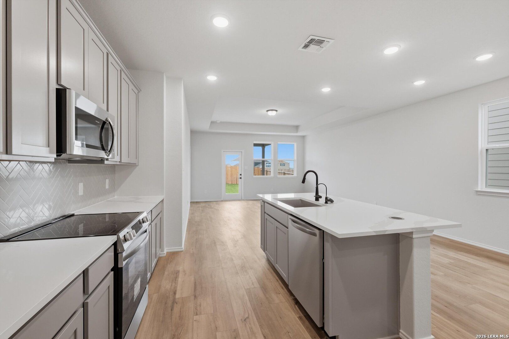 Modern open-concept kitchen with white quartz island, stainless appliances, subway tile backsplash in Davidson Homes The Blanco C, San Antonio