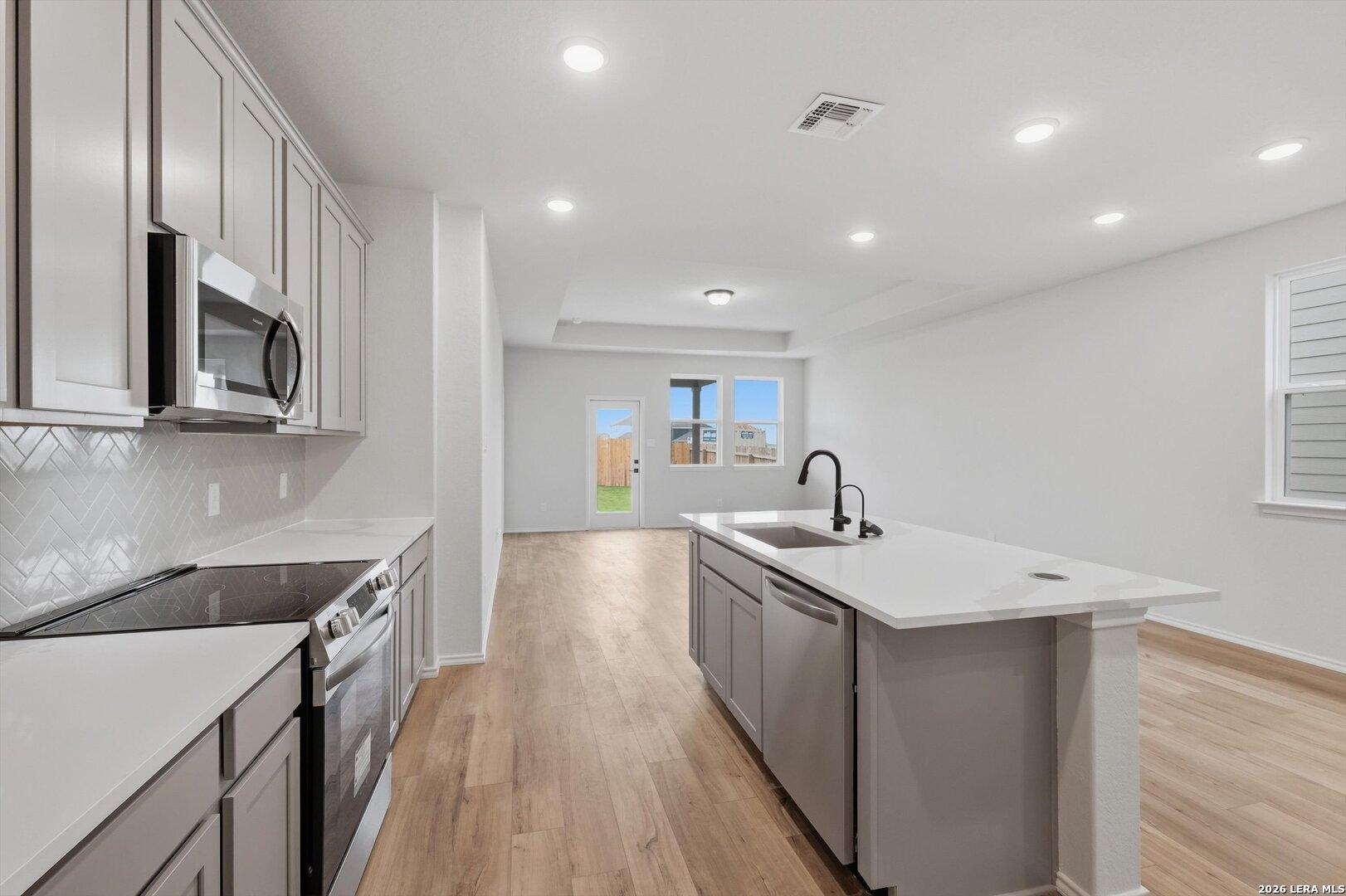 Modern open-concept kitchen with white quartz island, stainless appliances, subway tile backsplash in Davidson Homes The Blanco C, San Antonio