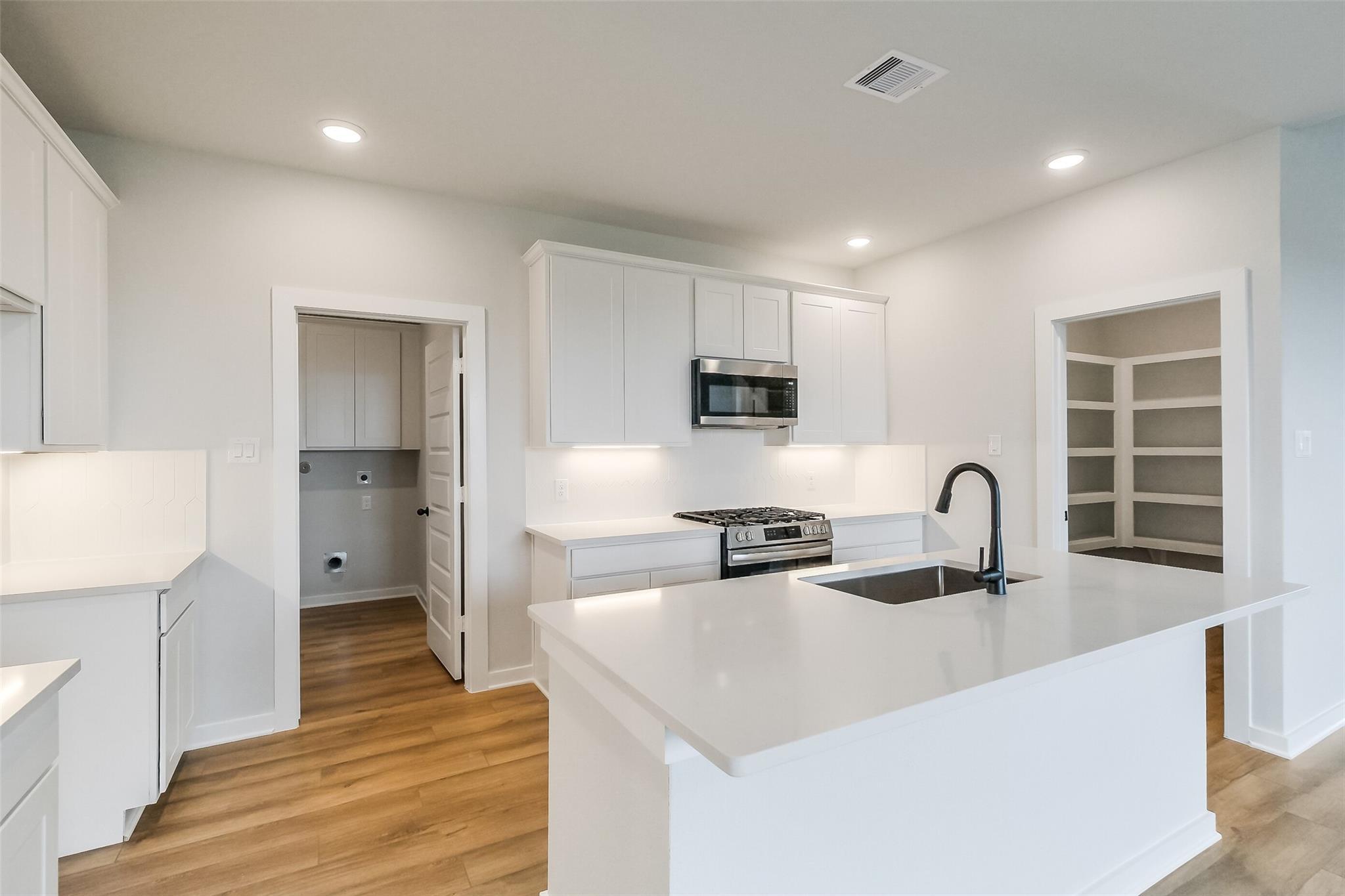 Modern white kitchen with quartz island, stainless appliances, and open layout in Davidson Homes The Tierra B, Beasley, Texas
