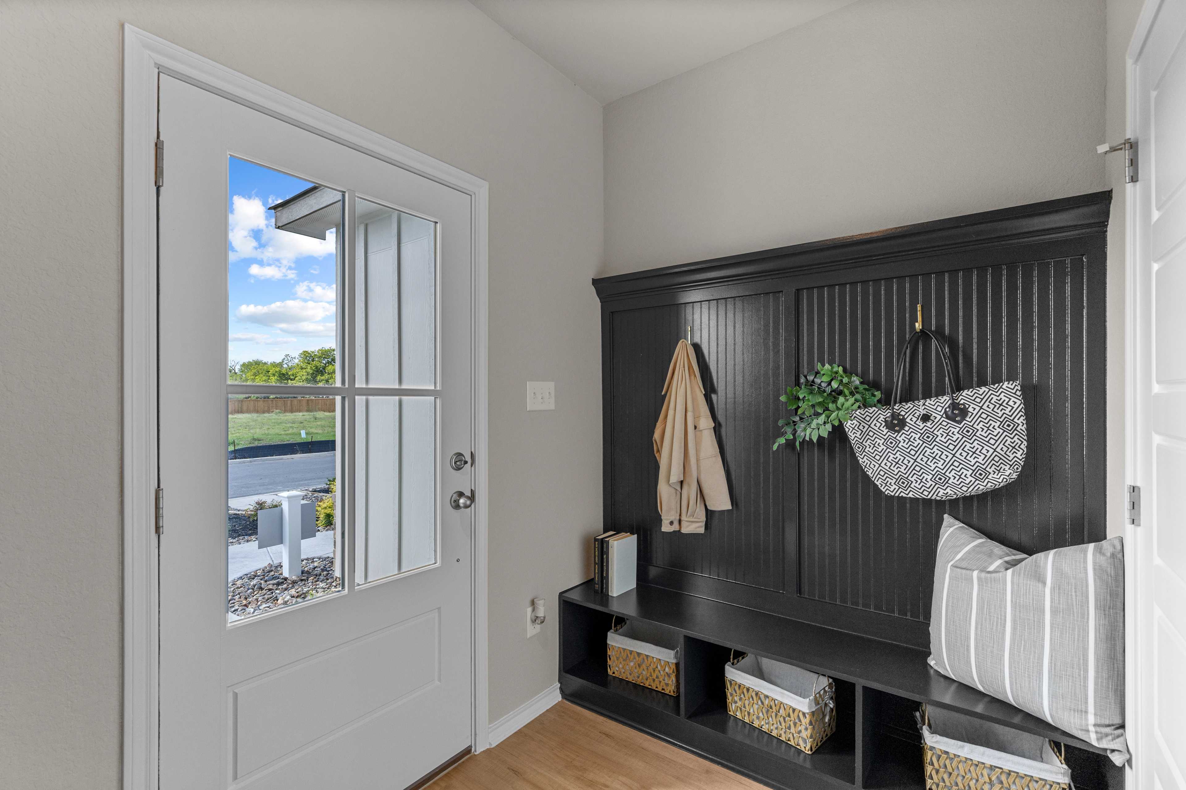 Inviting entryway in The Sabine C by Davidson Homes featuring dark wood coat rack with hooks, wicker baskets, and windowed front door with scenic outdoor view