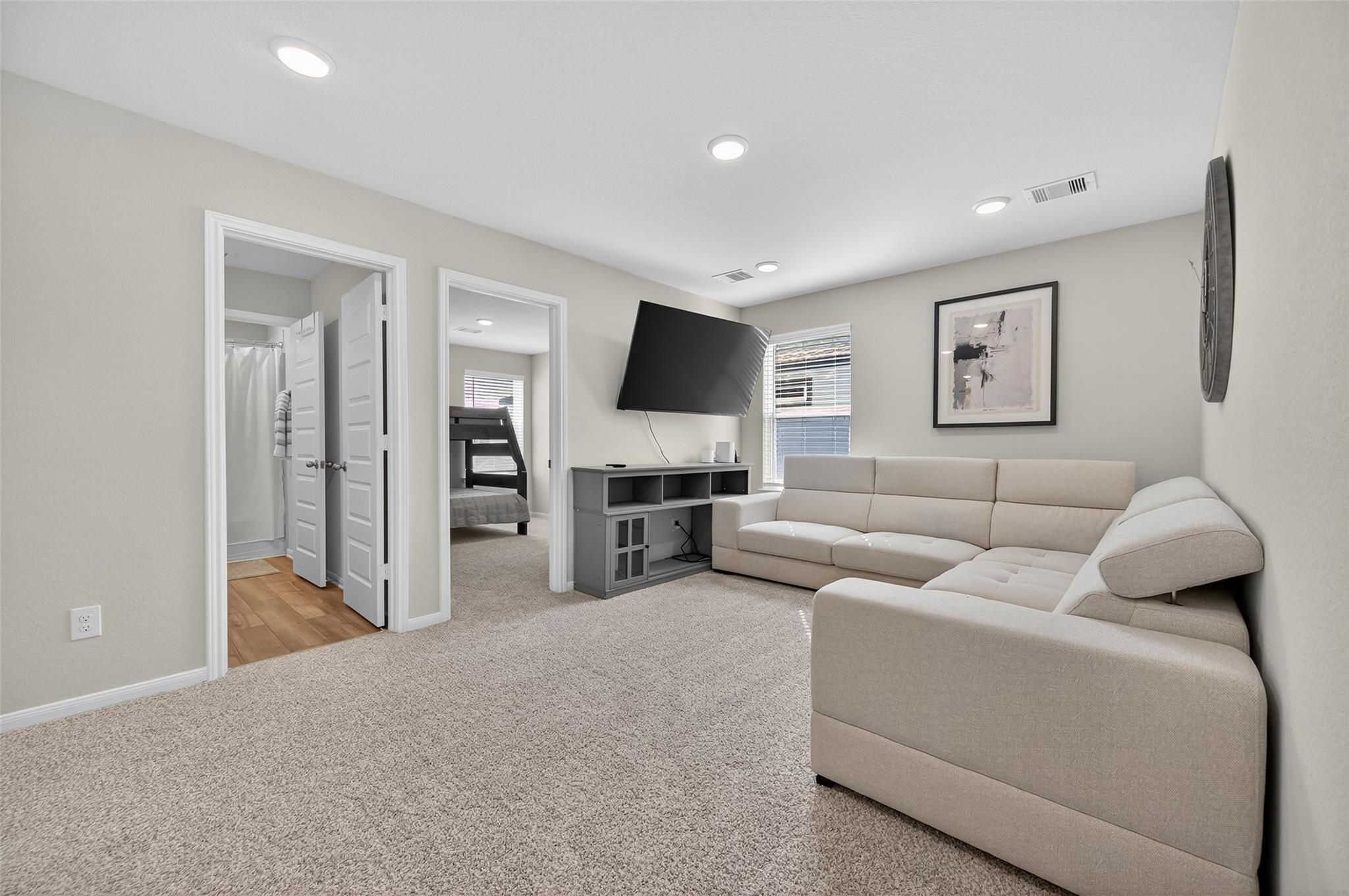 Cozy upstairs family room with beige sectional sofa, mounted TV, and bedroom access in 5-bedroom Davidson Homes The Brazos E, Magnolia Texas
