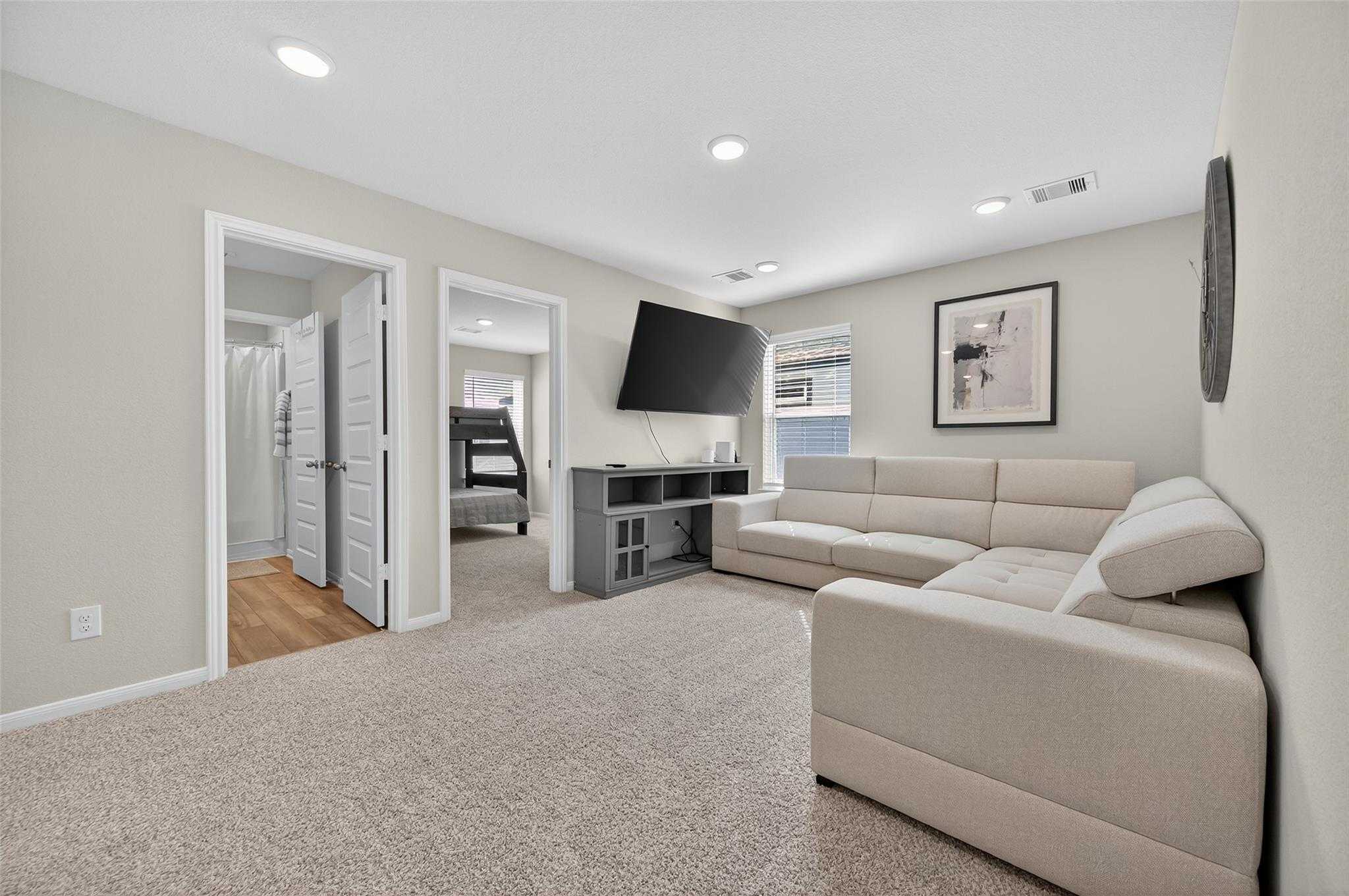 Cozy upstairs family room with beige sectional sofa, mounted TV, and bedroom access in 5-bedroom Davidson Homes The Brazos E, Magnolia Texas