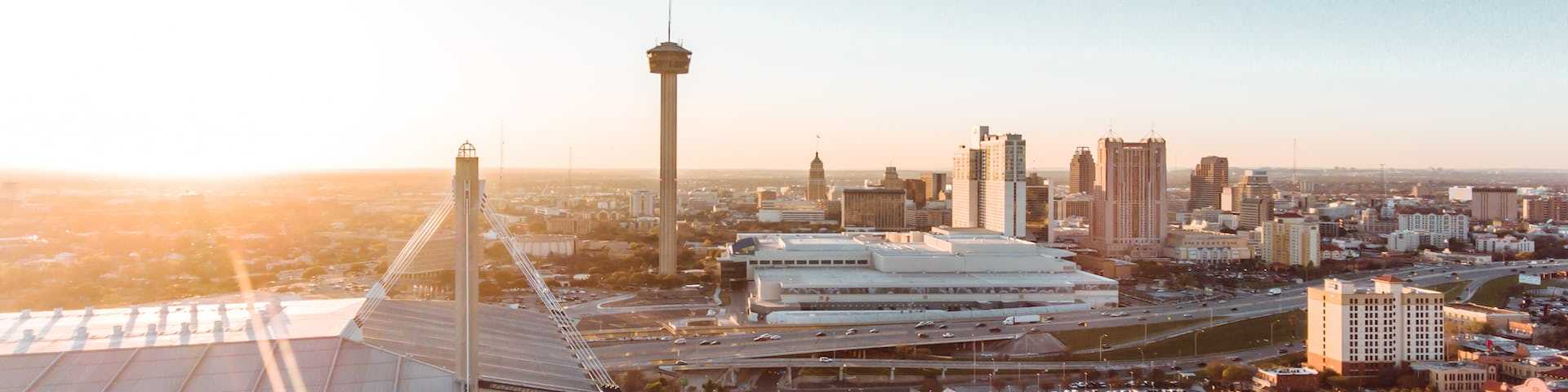 Aerial sunset view of San Antonio skyline with iconic Tower of the Americas, Alamodome, and urban neighborhoods