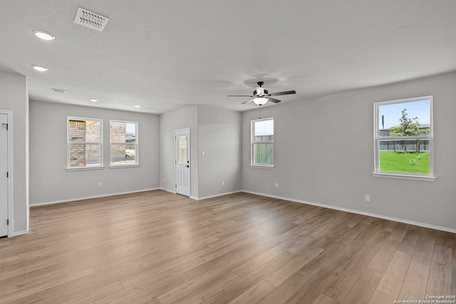Spacious living room with hardwood floors, ceiling fan, and large windows overlooking green lawn in The Daphne K 4-bedroom home, San Antonio