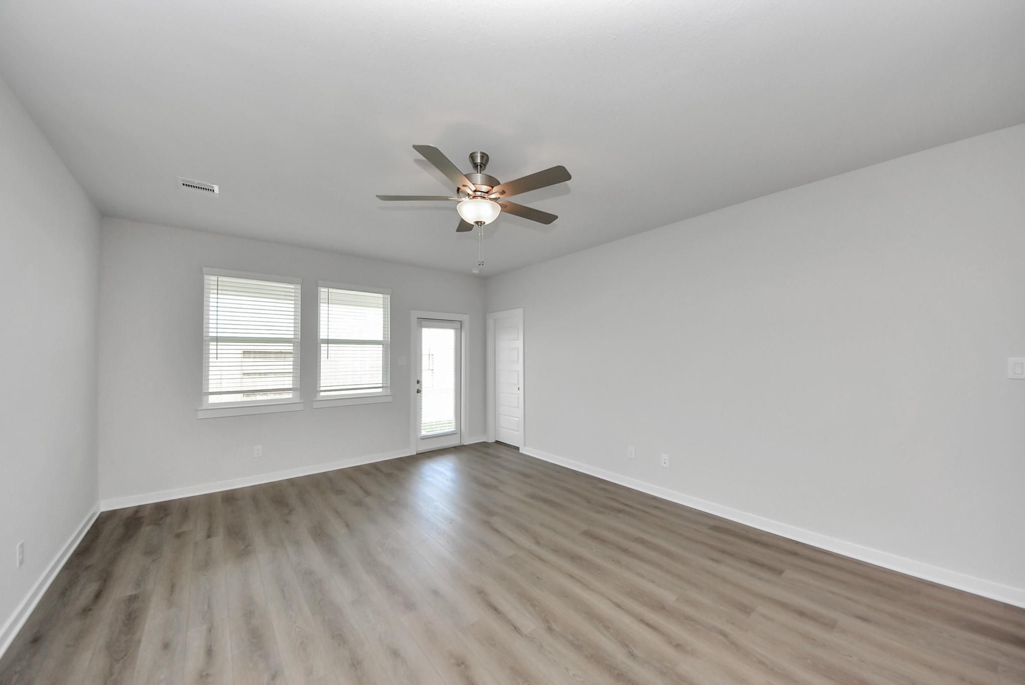 Bright empty room with wood-look flooring, ceiling fan, and blinds in Davidson Homes San Marcos E plan, Emberly, Beasley, TX
