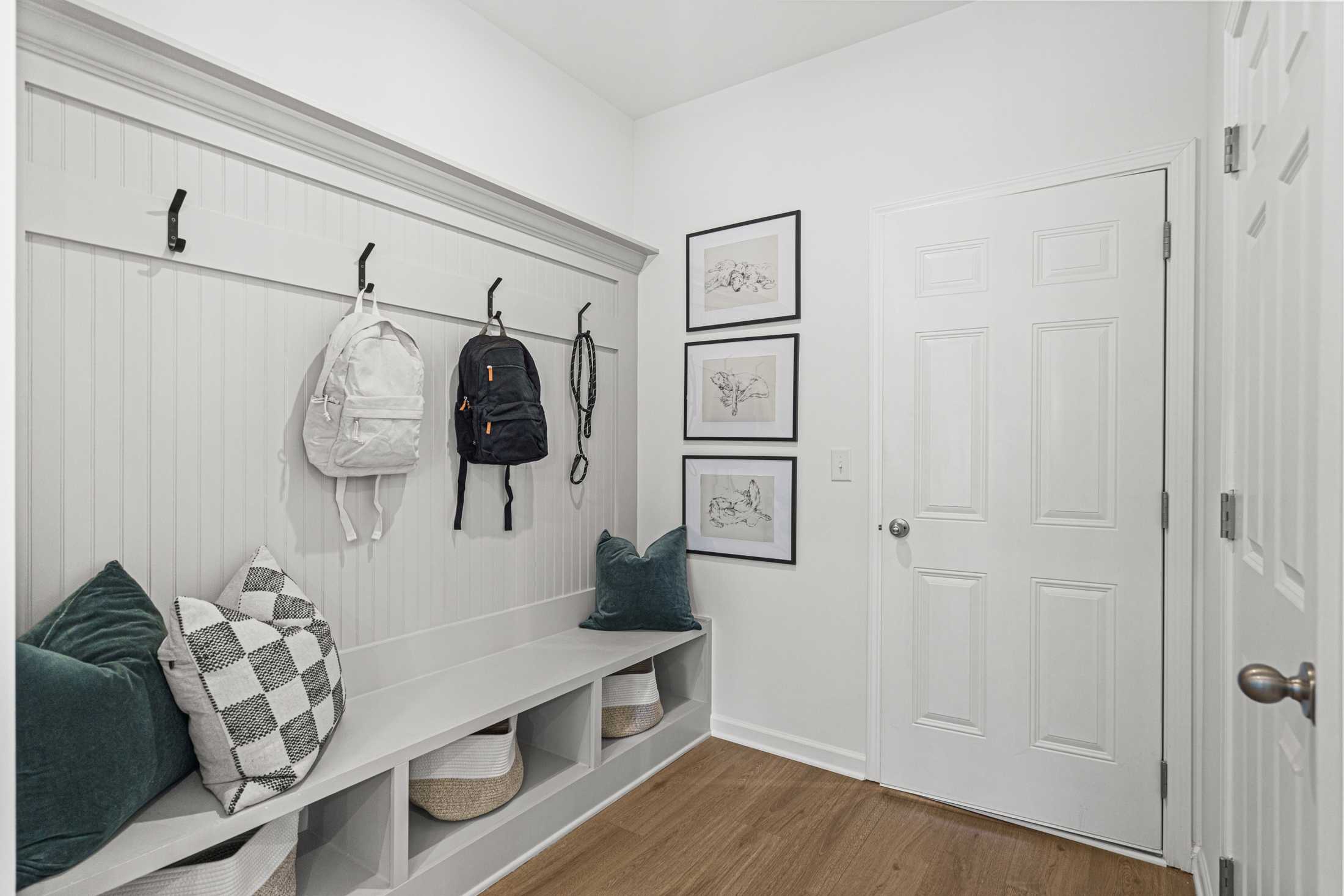 Cozy mudroom in The Hickory A featuring wainscoted walls, backpack hooks, cushioned bench with storage, and framed art in Hoschton GA home