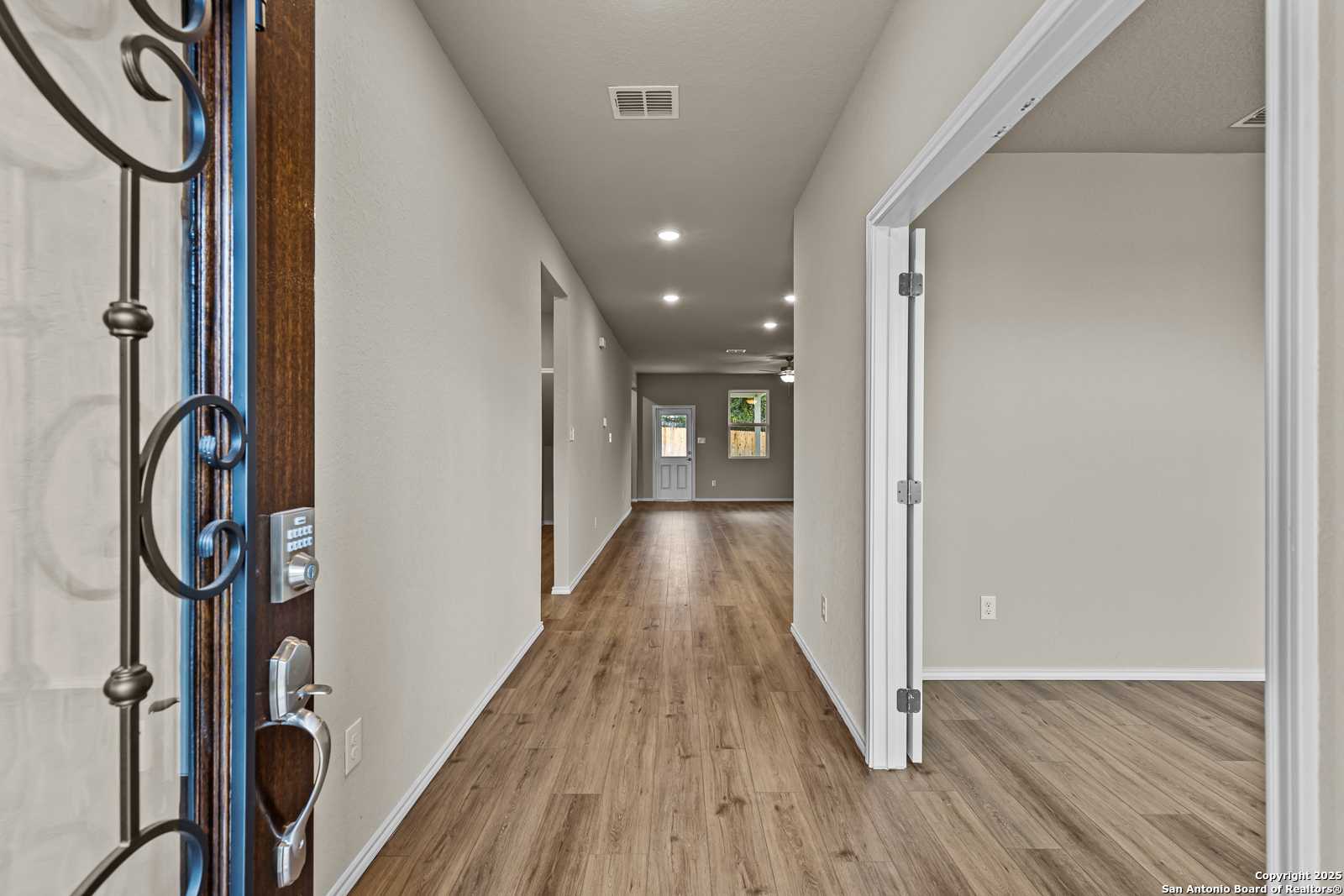 Grand entry hallway with ornate wooden door, hardwood floors, and open doorways in Davidson Homes The Douglas F, San Antonio