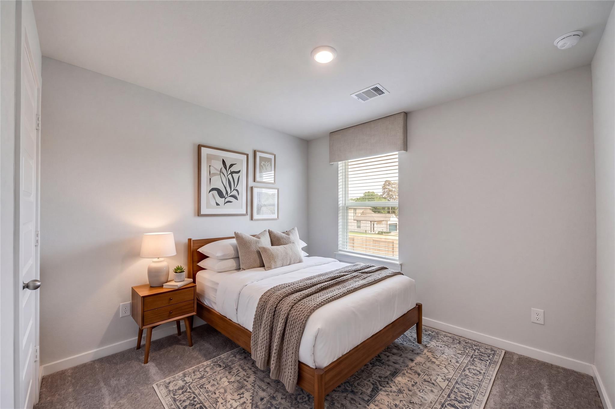 Bright bedroom with wood bed frame and nightstand in Davidson Homes' The Brazos F, Liberty Estates, Cleveland, Texas