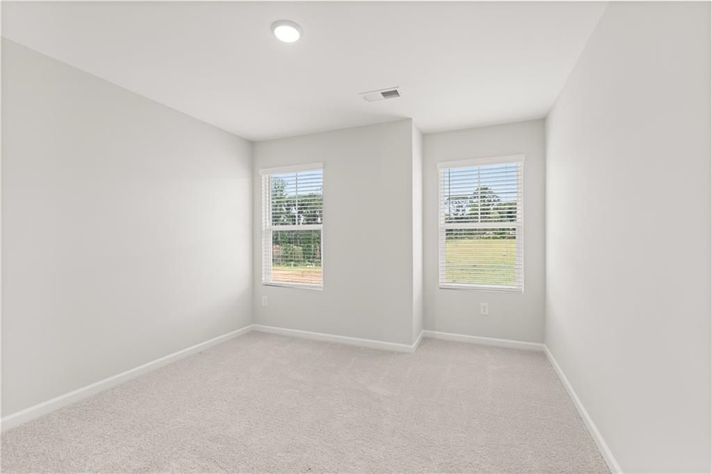 Bright, carpeted bedroom with neutral walls and windows in The Wake B floor plan at Hemingway, Cumming, Georgia.