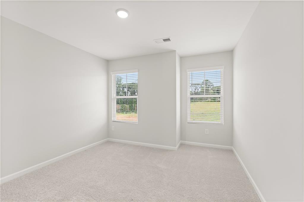 Bright, carpeted bedroom with neutral walls and windows in The Wake B floor plan at Hemingway, Cumming, Georgia.