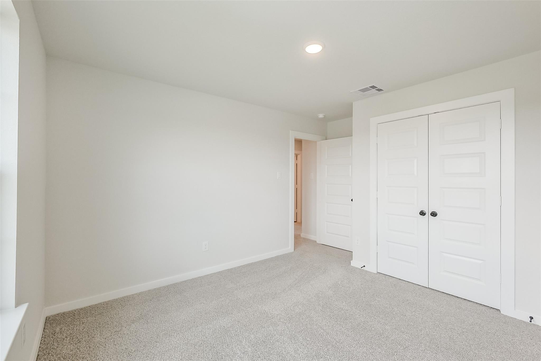 Bright secondary bedroom with white walls, beige carpet, bi-fold closet doors in Davidson Homes Tierra B, Emberly, Beasley, Texas
