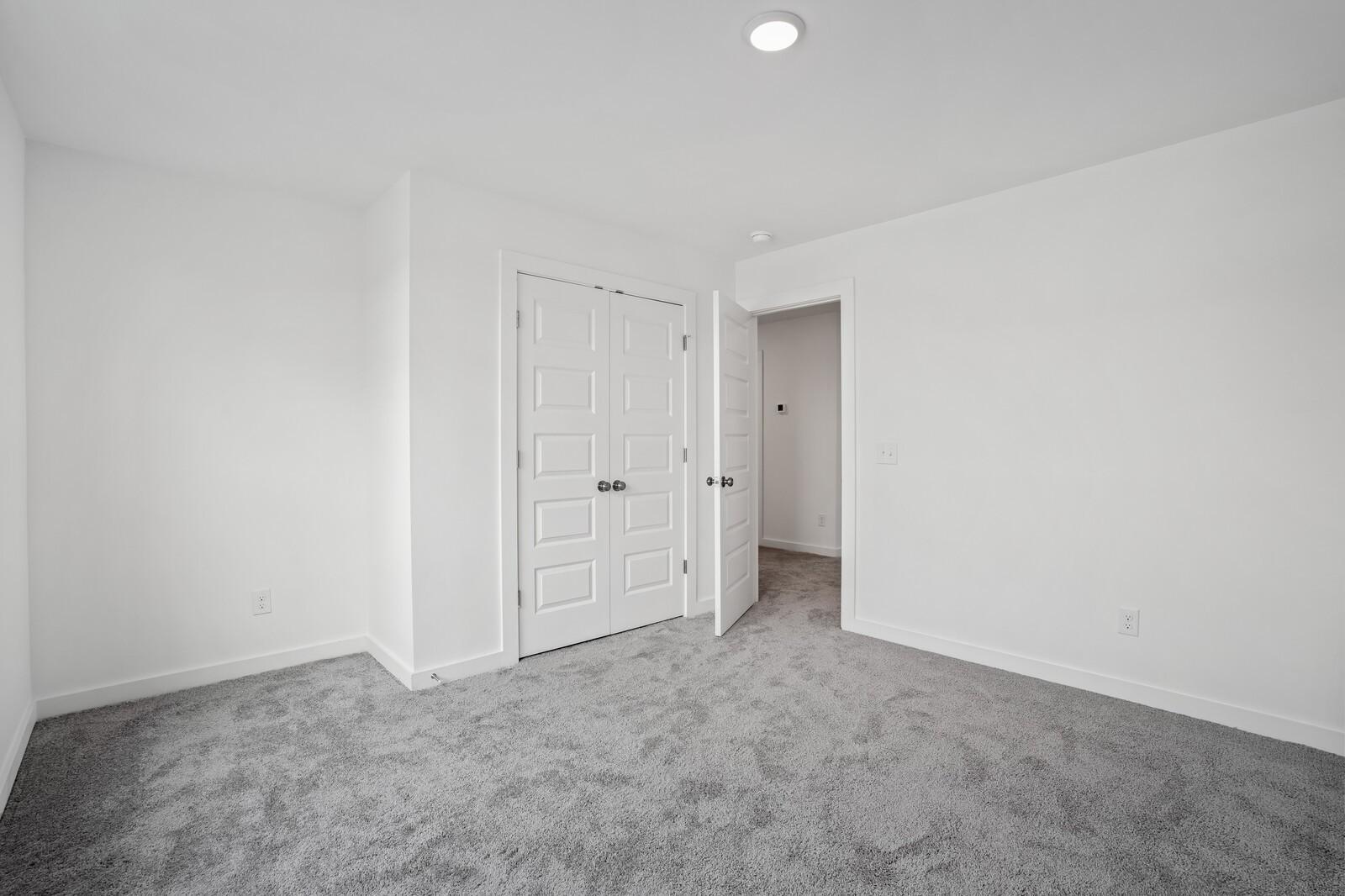 Bright bedroom with gray carpet and closet doors in The Logan C floor plan at Calista Farms, White House, Tennessee.