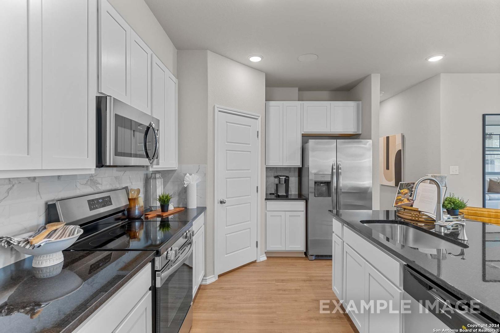 Modern kitchen with white shaker cabinets, stainless steel appliances, granite counters in Davidson Homes Sabine B, San Antonio TX