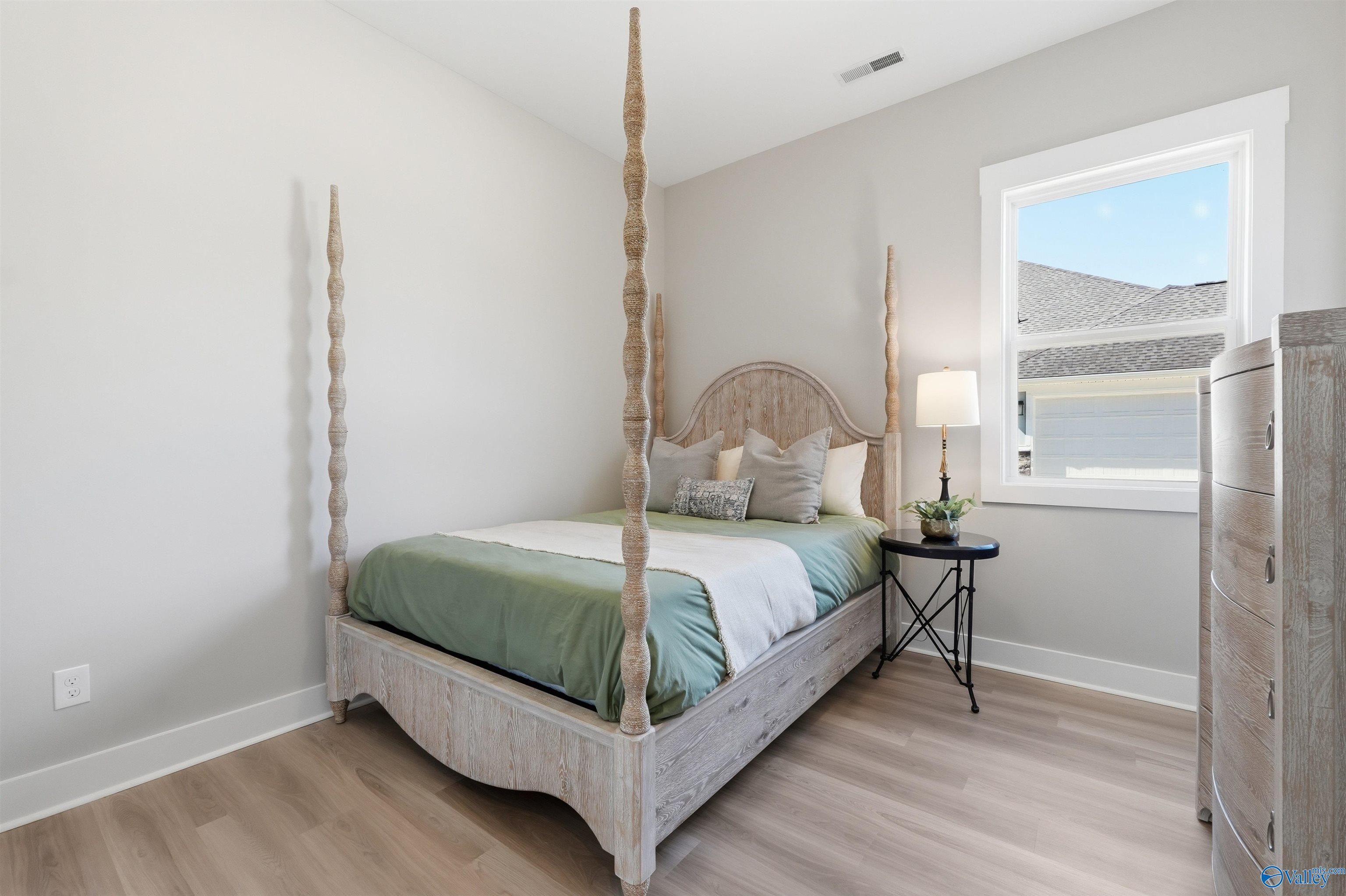 Cozy bedroom with whitewashed four-poster bed, green duvet, pillows, lamp, and dresser in Evermore Homes The Oxford B, Owens Cross Roads, Alabama