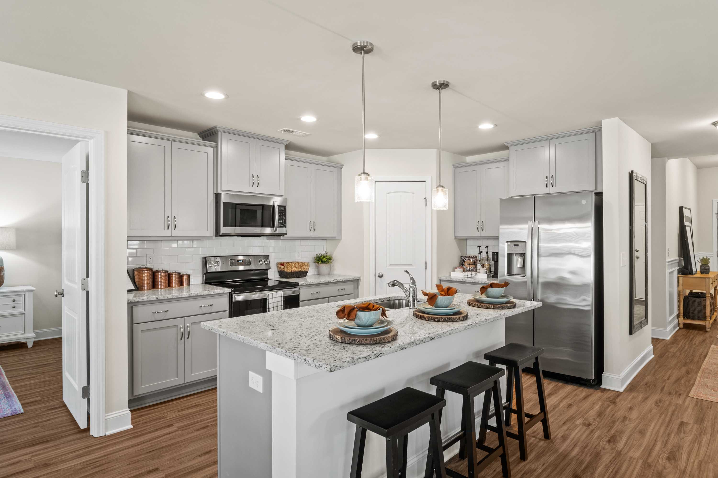 Modern open-concept kitchen in Berry Cove, New Market AL with white shaker cabinets, granite island, stainless appliances and hardwood floors