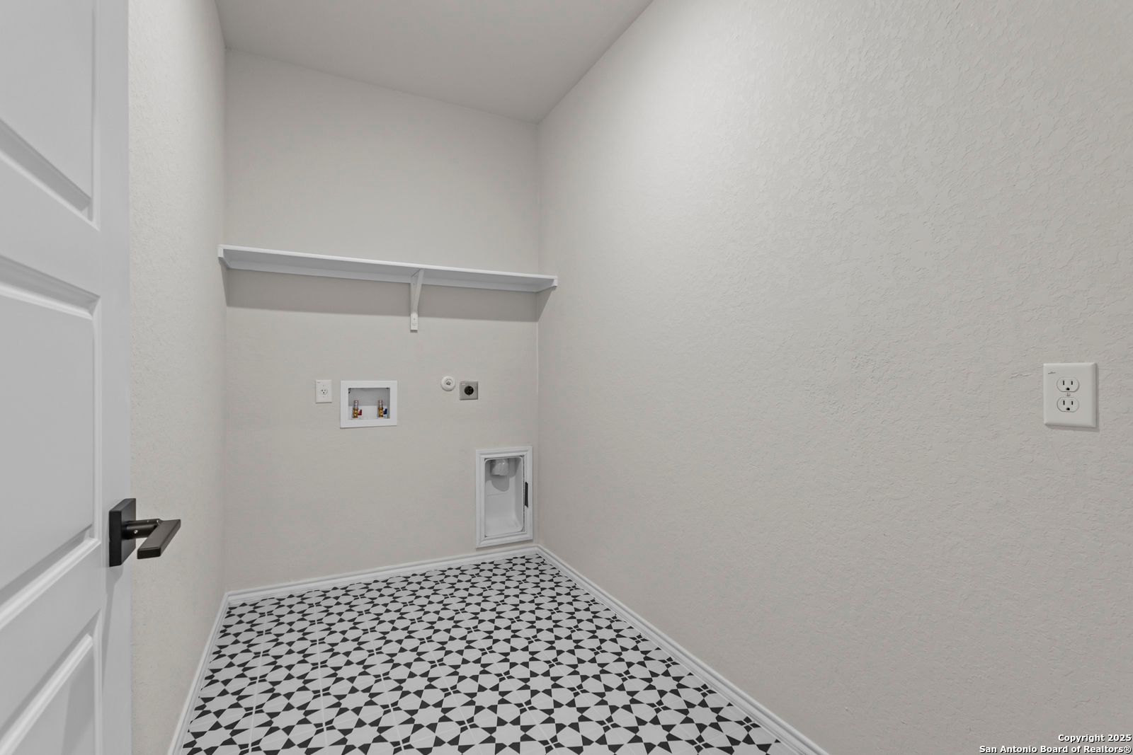 Functional laundry room with washer/dryer hookups, storage shelf, cabinet, and geometric tile floor in Davidson Homes The Douglas C, Seguin, Texas