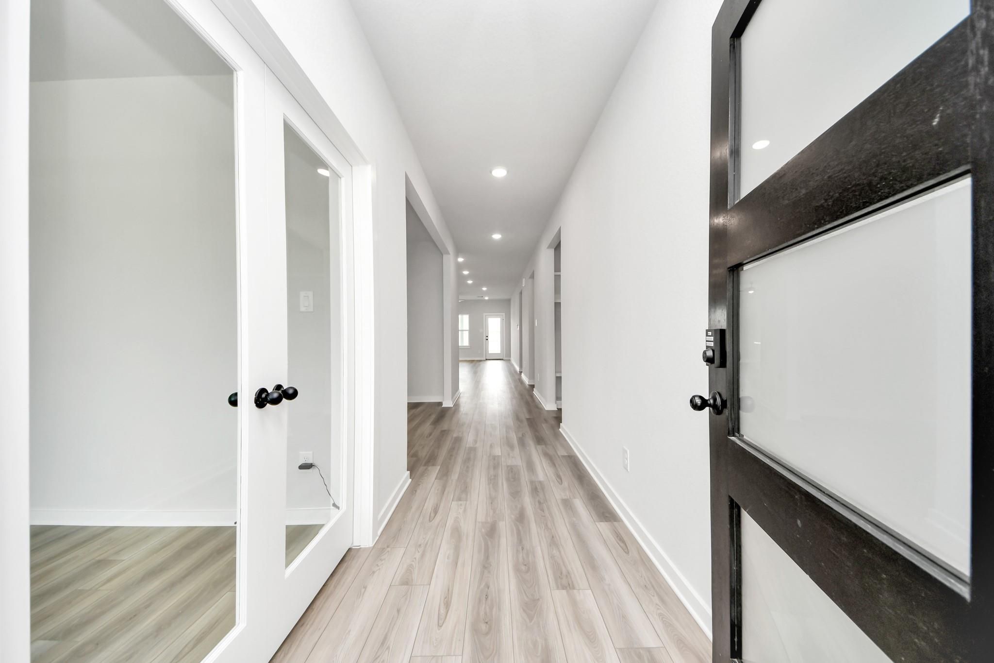 Bright hallway with wood-look flooring and modern glass doors in The Sorrento E floor plan by Davidson Homes in Crosby, TX.