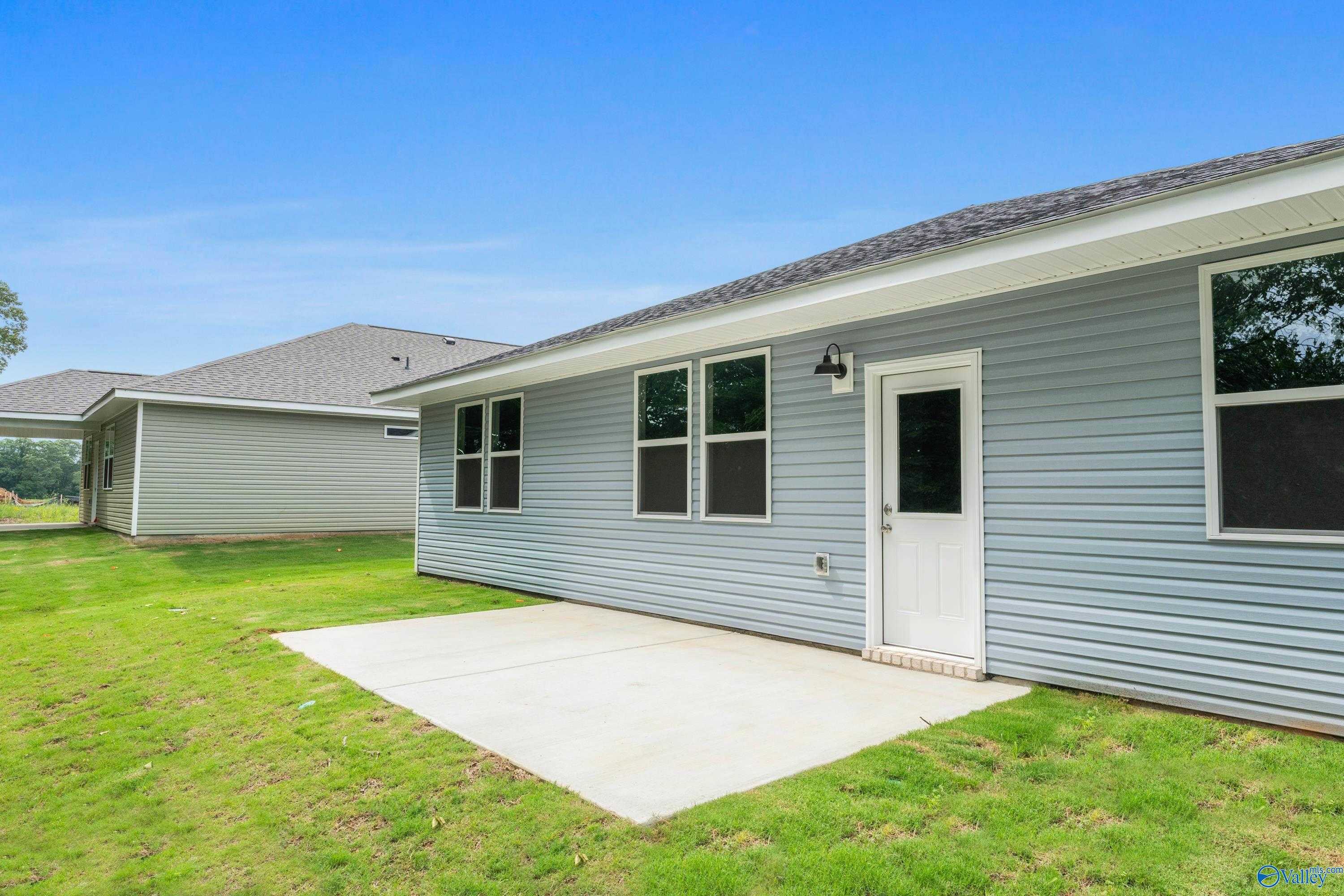 Side view of light blue single-story The Phoenix home with windows, door, concrete patio, and lush green yard in Bailey Park, Fayetteville, TN