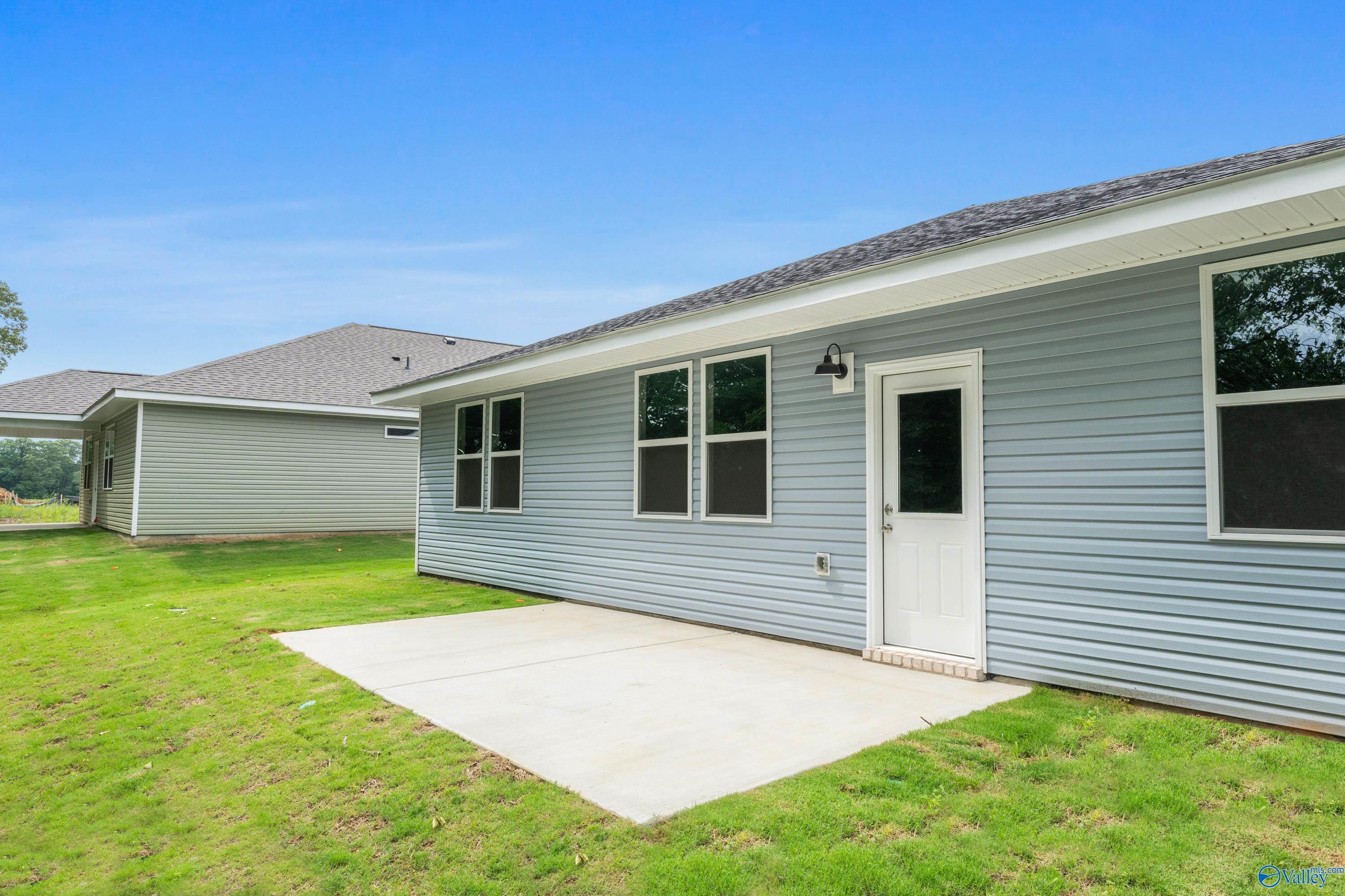Light blue single-story home side exterior with entry door, windows, and concrete patio in lush green yard, Davidson Homes The Phoenix, Fayetteville, TN