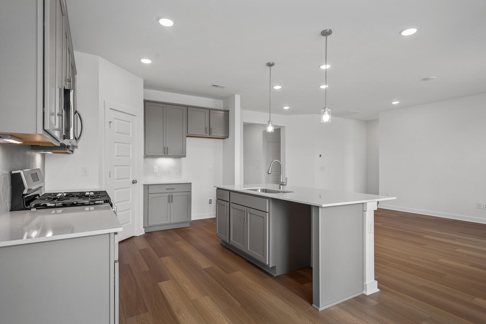 Modern kitchen in The Asheville home with gray shaker cabinets, white quartz island, gas range, and pendant lighting