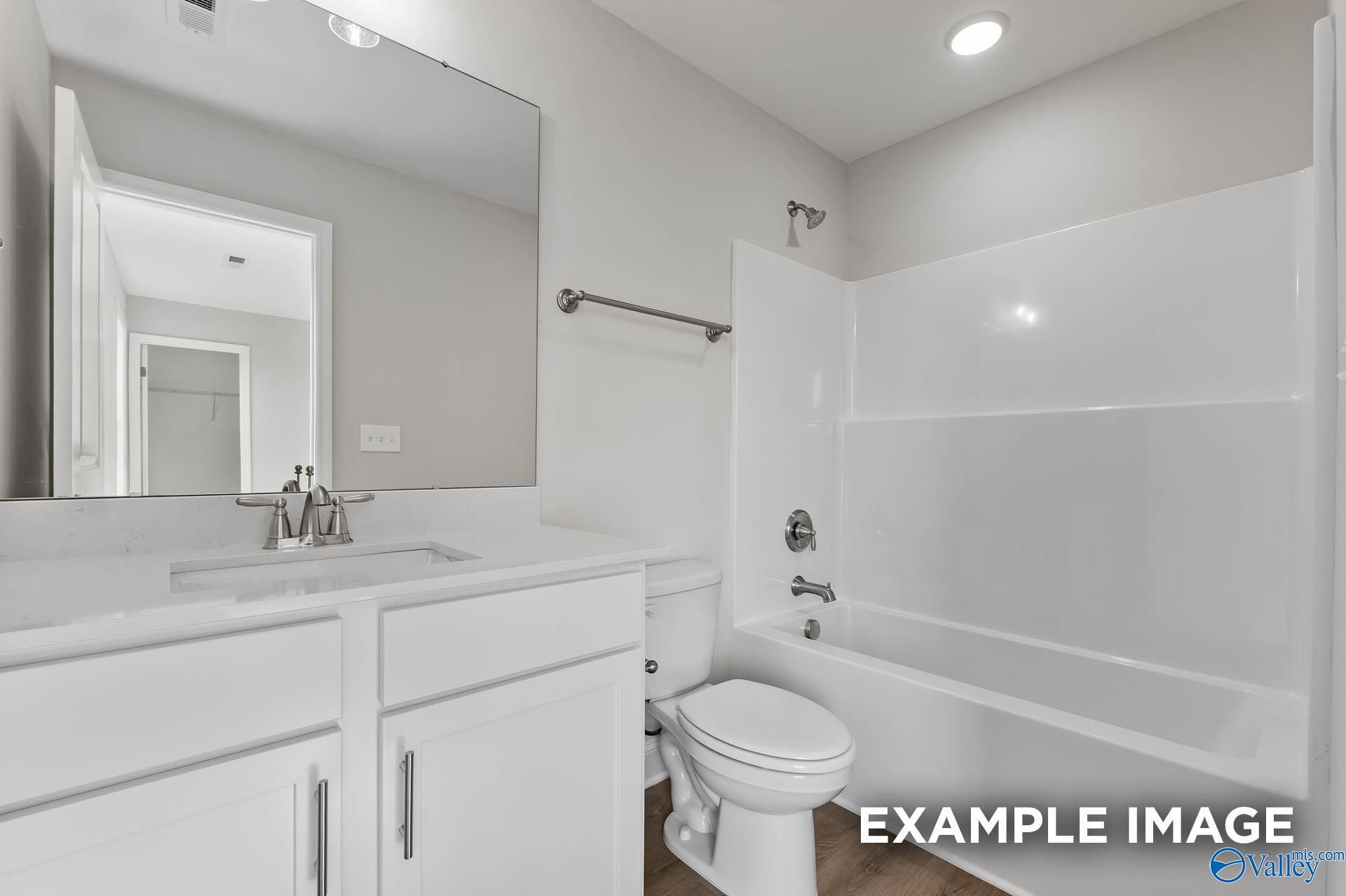 Bright bathroom with white vanity, single sink, large mirror, alcove tub shower, and toilet in Davidson Homes Chelsea D, New Market, AL